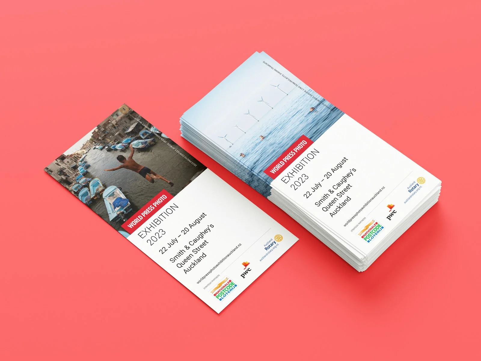 Stacks of exhibition flyers on a pink background showing images of a person jumping in a flooded street and wind turbines in the ocean.
