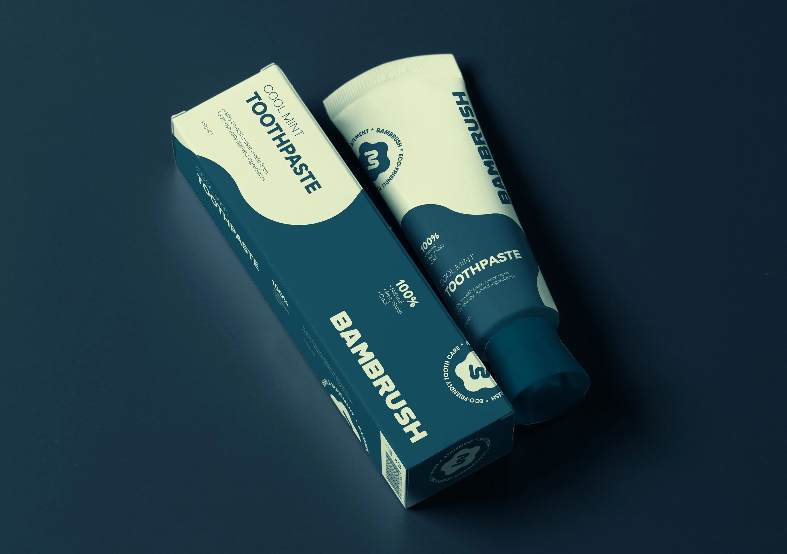 A tube of Bambrush cool mint toothpaste next to its box, both placed on a dark surface. The packaging is blue and white, with text indicating it is 100% natural and eco-friendly.
