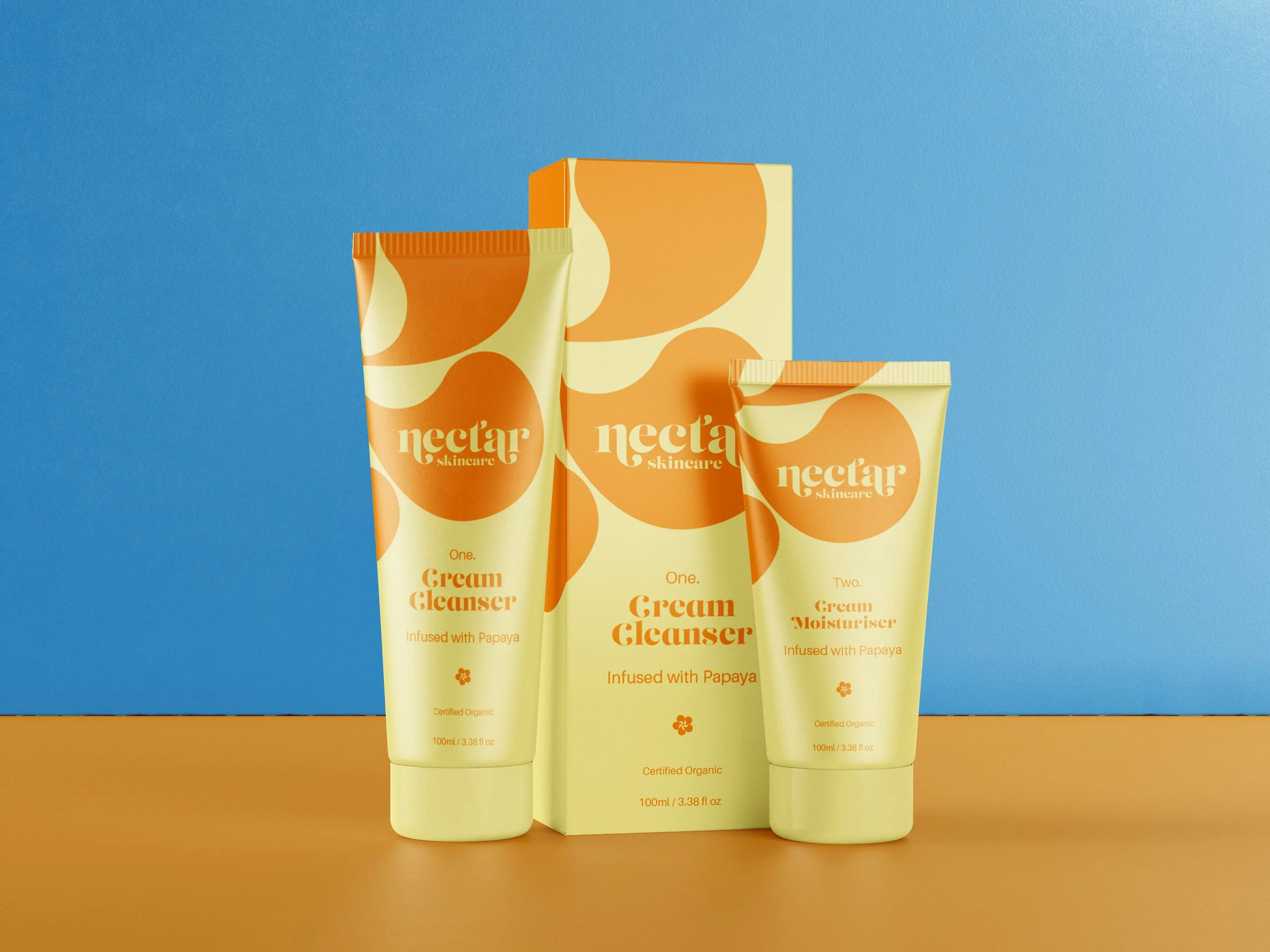 Two tubes and a box of Nectar skincare products, including a cream cleanser and a moisturizer, with packaging in yellow and orange colors on a two-toned background of blue and orange.