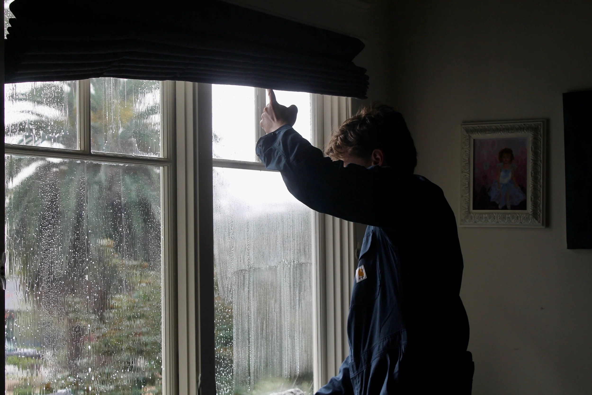 Person cleaning a window with a cloth on a rainy day inside a room.