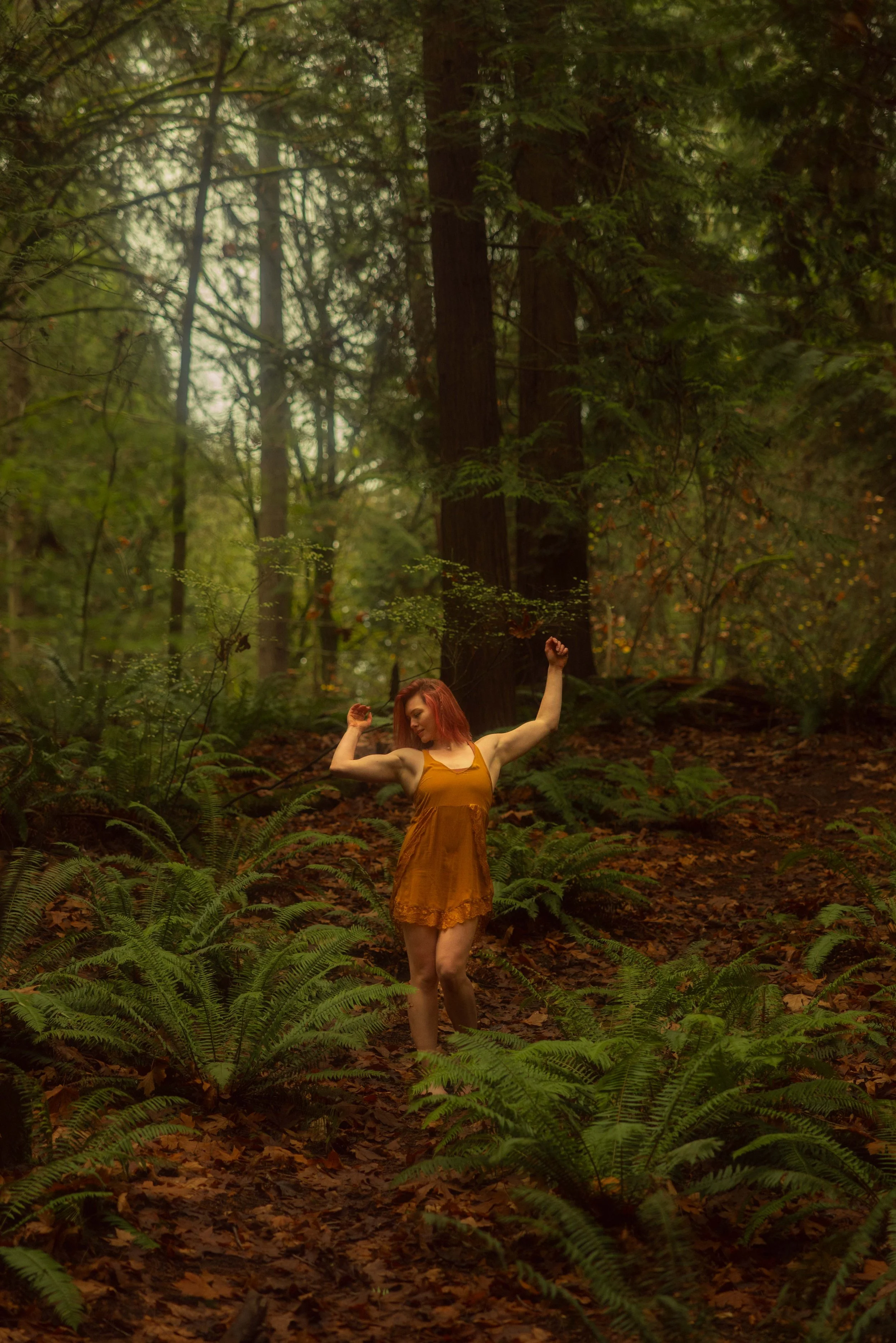 A women in a dark yellow dress dancing through the woods.