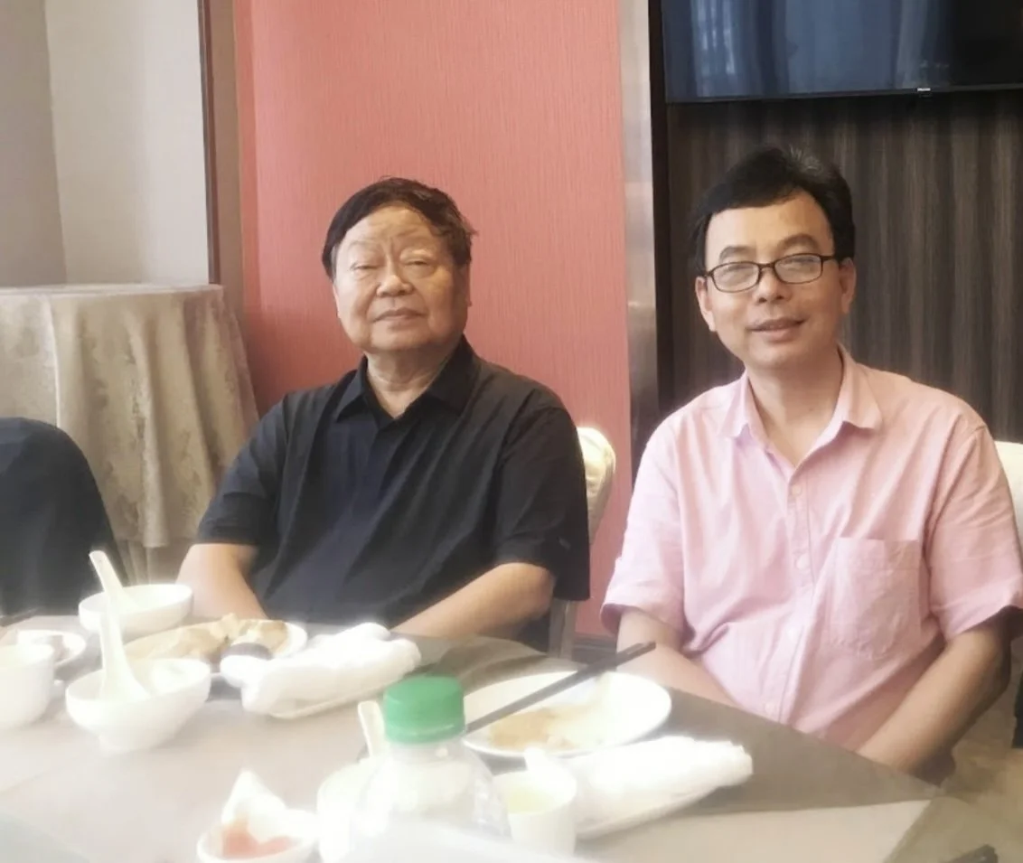 Two men sitting at a dining table in a restaurant with tableware and food remnants visible.