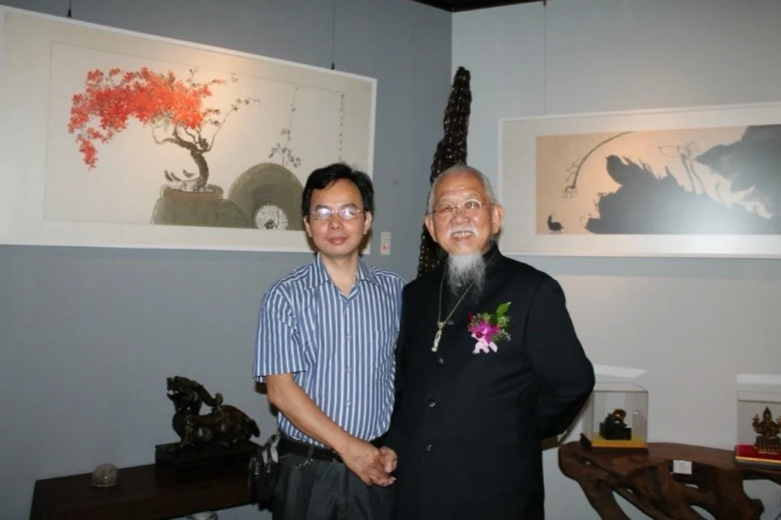 Two men shaking hands in an art gallery, with traditional Asian calligraphy and paintings on the wall behind them.