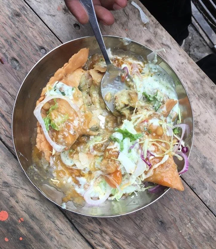 Food on Foot tour in Lahore with karakoram Bikers. A food plate with Samosa chaat food, including puffed fried bread, chopped vegetables, chickpeas, and a mix of sauces and yogurt, on a wooden table.