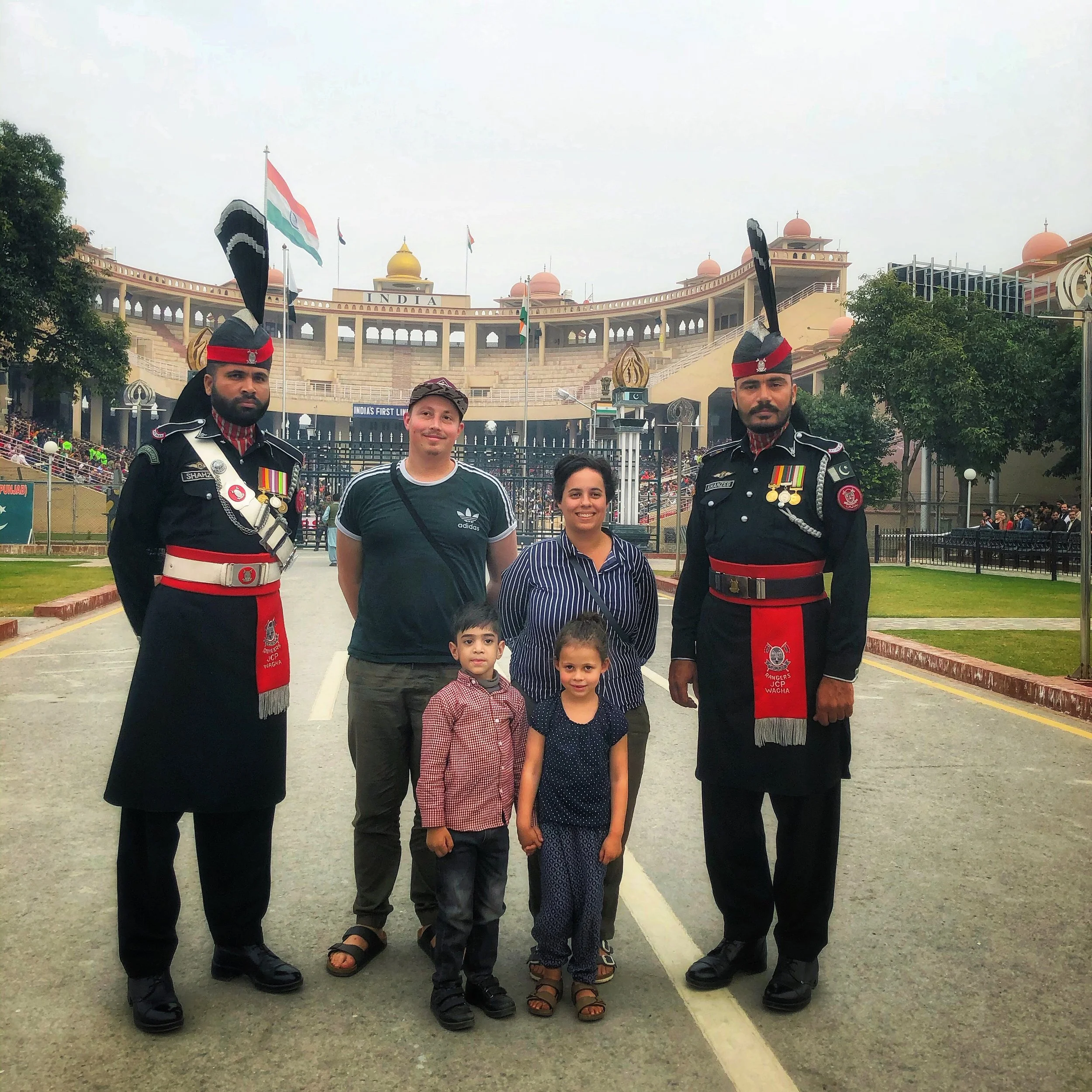 A family of five posing with two soldiers in ceremonial uniforms outside a government building in India.