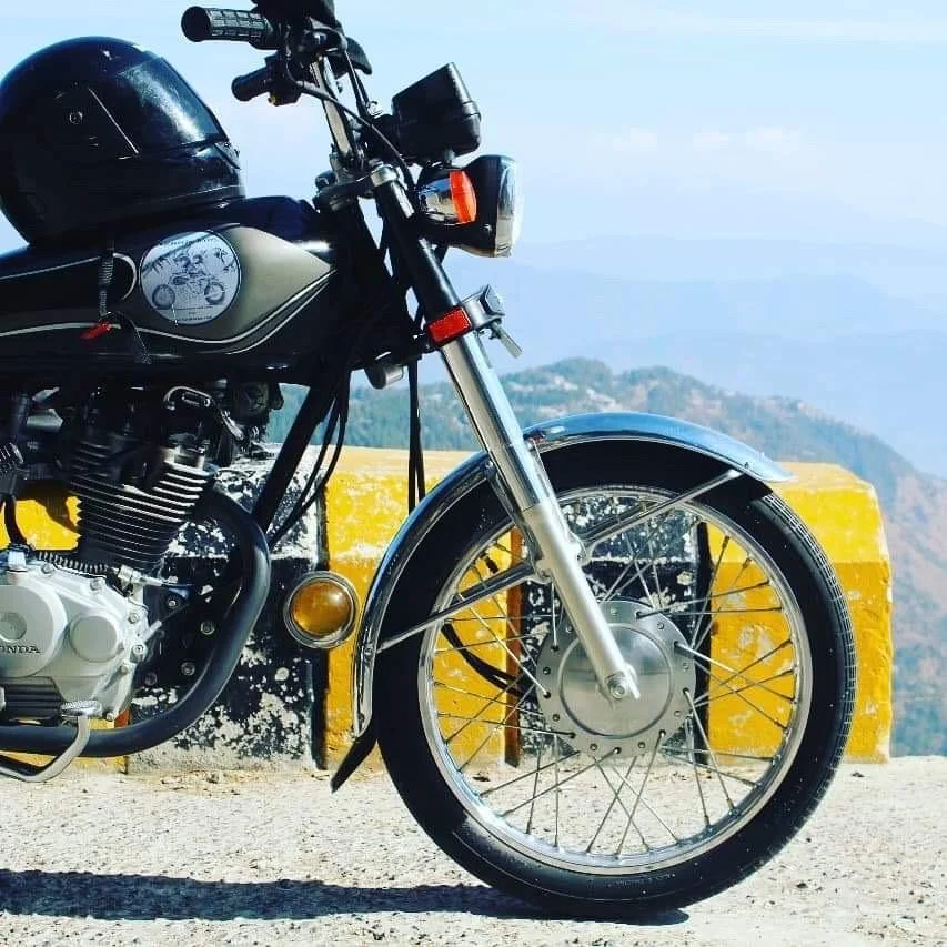 A vintage black Honda motorcycle parked on a roadside with mountains and sea in the background.