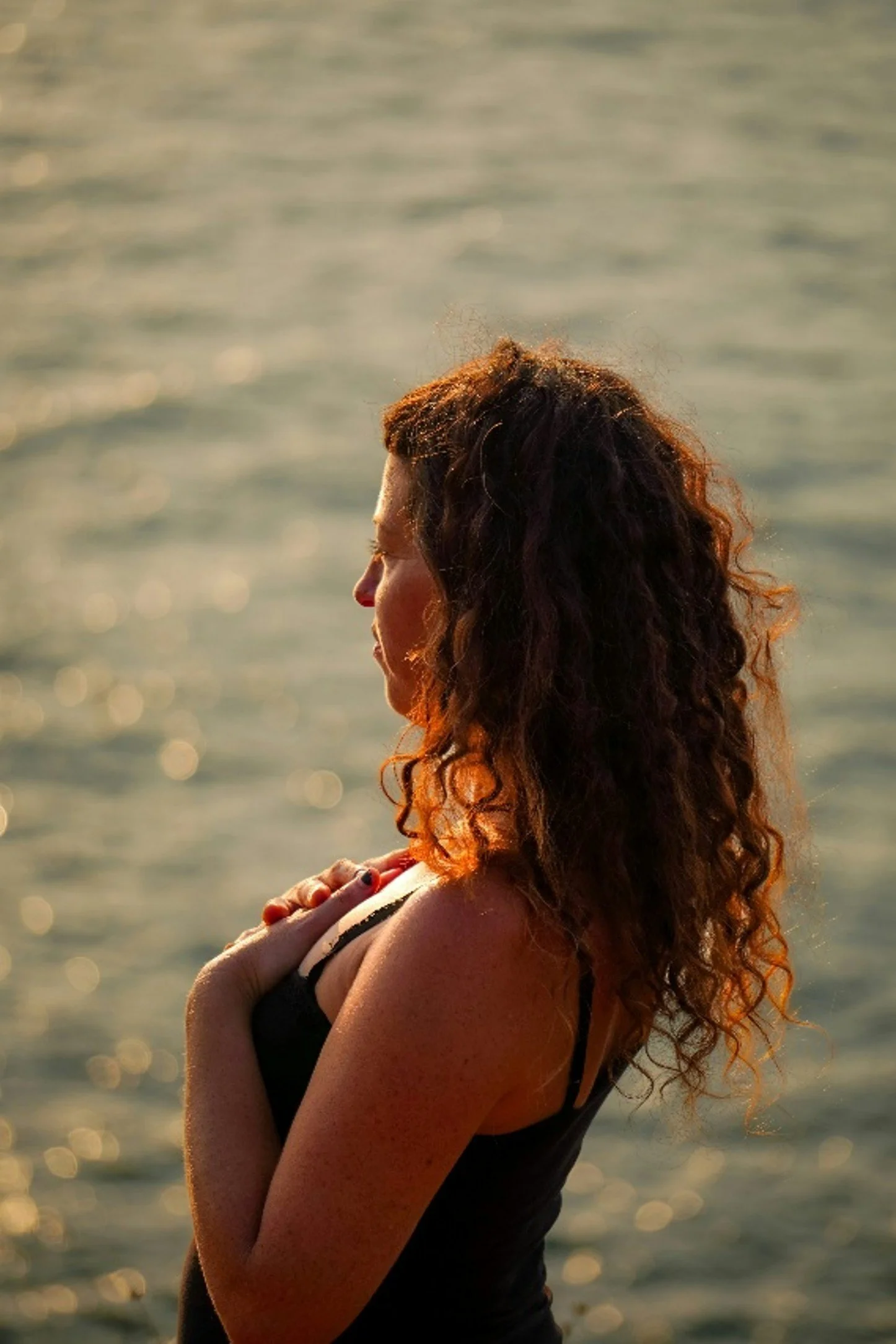 white jade holistic health  woman with curly hair stands near the water's edge enjoying the peaceful view of the surrounding nature transformation session psychk