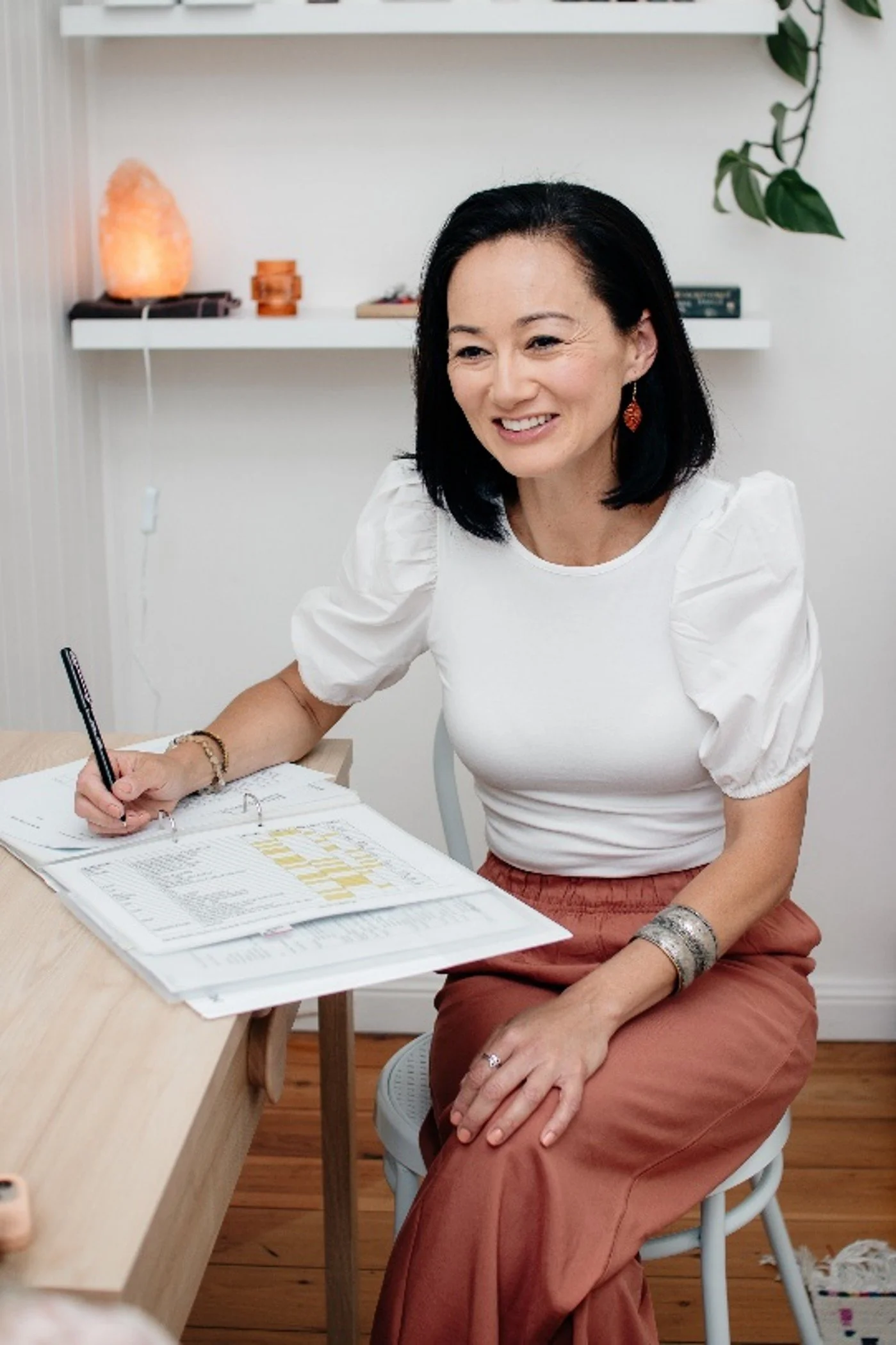 white-jade-holistic-health-founder-melissa-bergin-smiling-while-writing-consultation-notes-in-clinic-for-kinesiology-mind-body-medicine-new-south-wales-cropped
