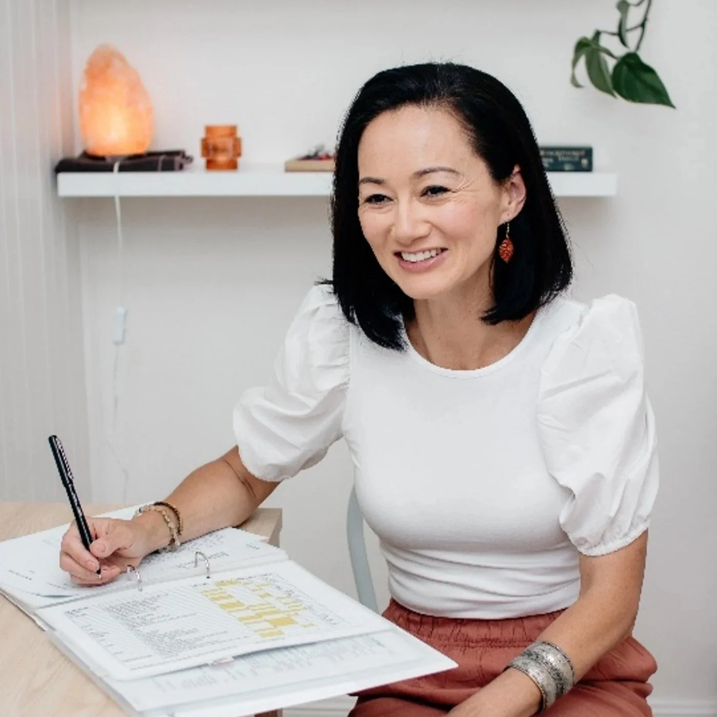 white-jade-holistic-health-founder-melissa-bergin-smiling-while-writing-consultation-notes-in-clinic-for-kinesiology-mind-body-medicine-new-south-wales