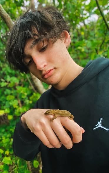 Young person holding a small frog on their hand outdoors