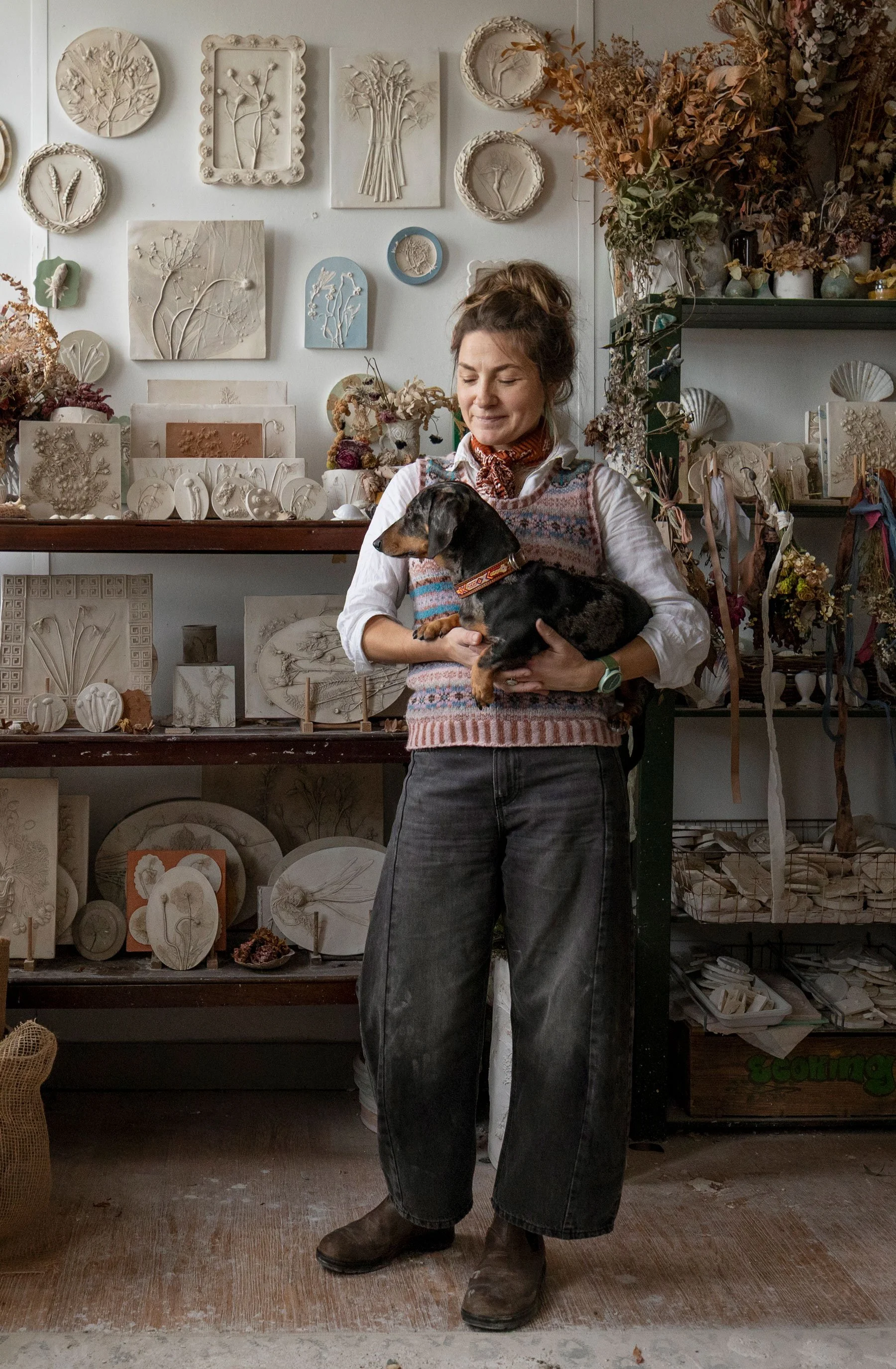 Portrait of artist Katy Eccles with her dog in her studio with botanical casts lining the walls and shelves