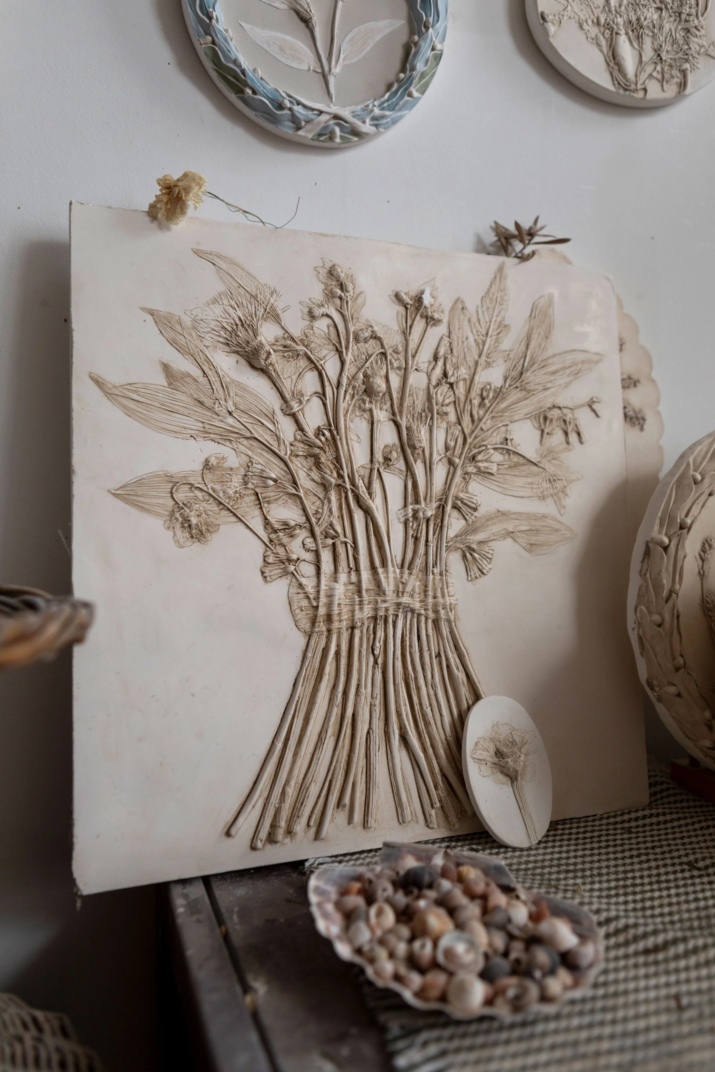 A botanical plaster cast of a vase with flowers and leaves, displayed on a table with seashells in the foreground.