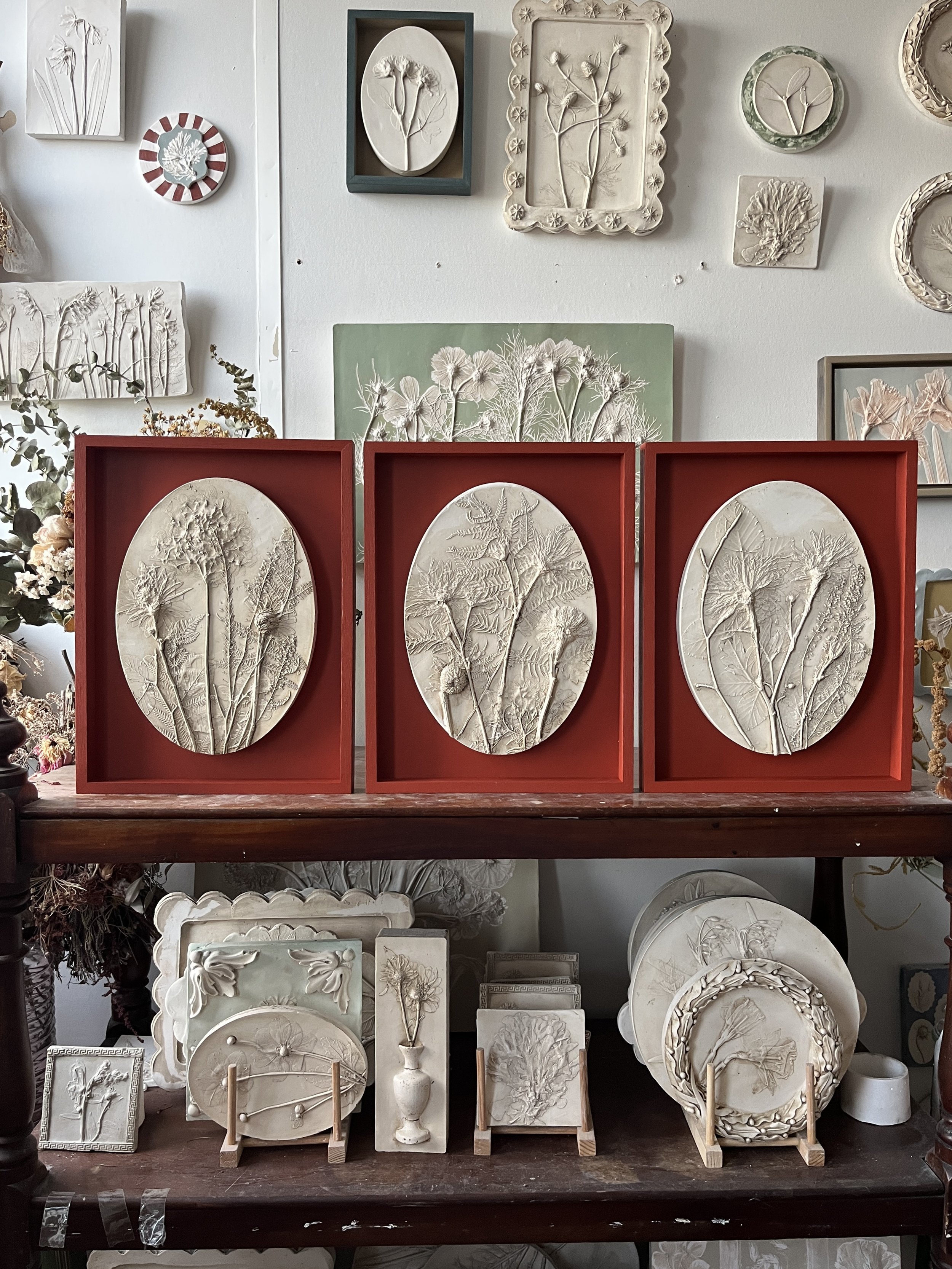 A trio of framed oval plaster casts of wedding flowers as a bespoke wedding flower commission, framed in red