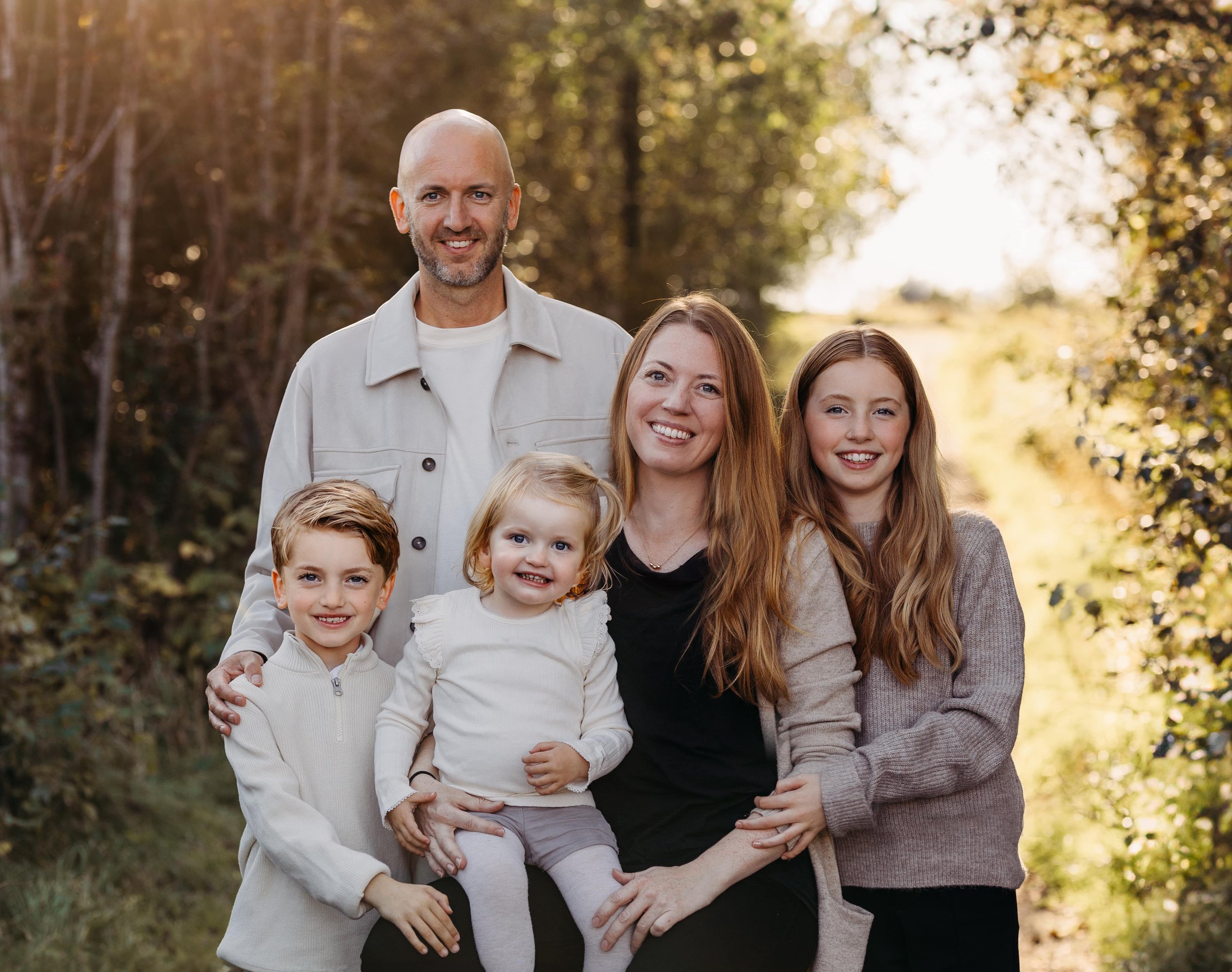 En familie på fem poserer ute i en skog. To voksne og tre barn, alle smiler.