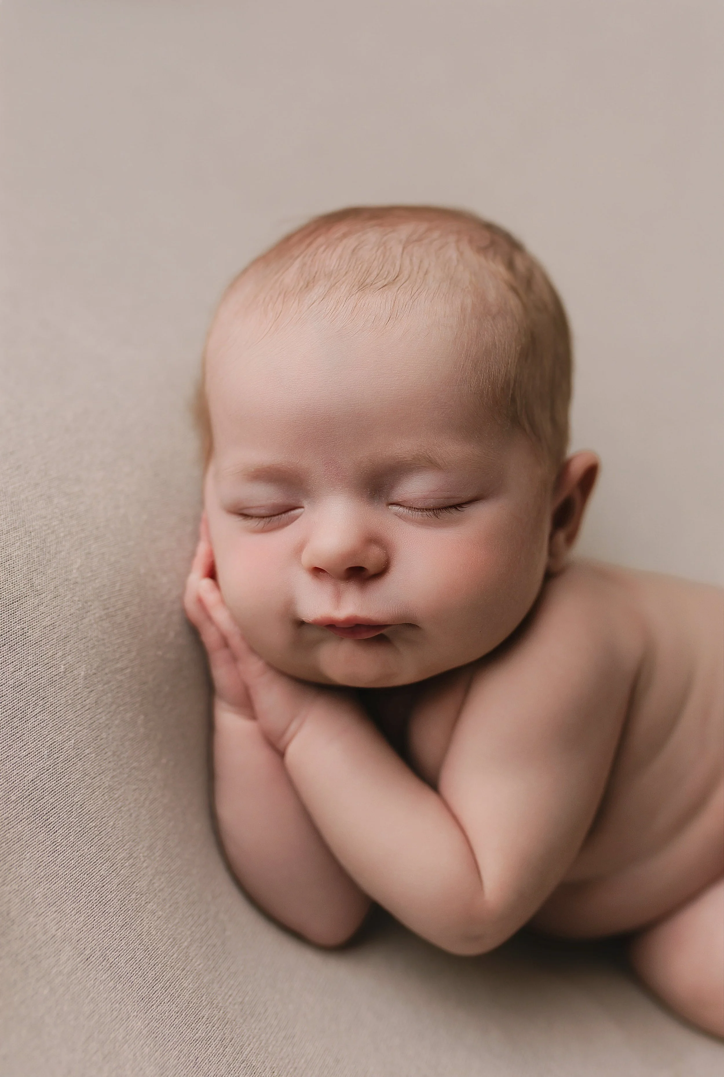 Nydelig sovende baby med lukket øyne, hvit hud og kort, lyst hår, hvilende hodet på en beige pute.