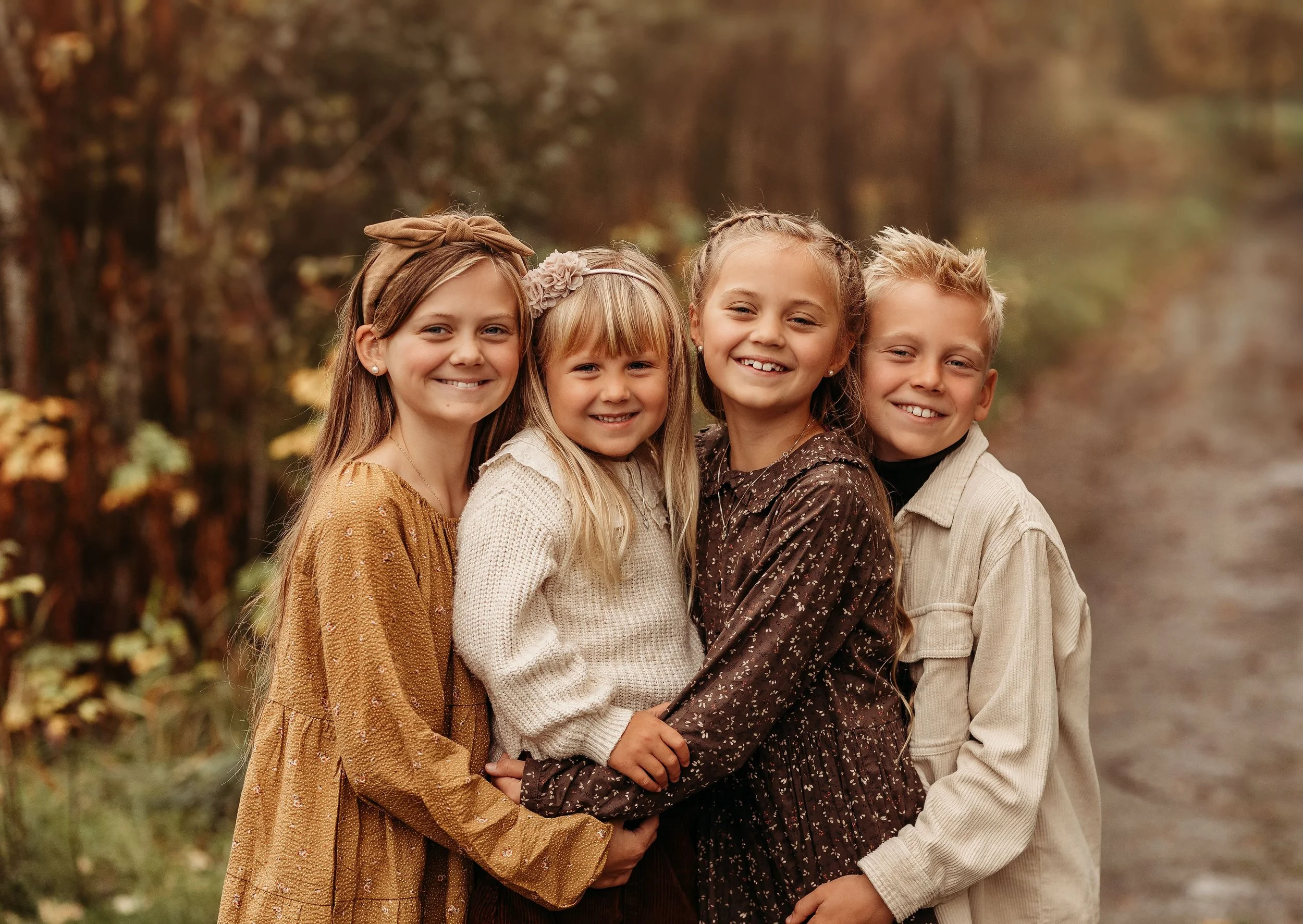 Fire barn står sammen på en skogssti med høstfarger i bakgrunnen, smilende og kledd i høstklær.