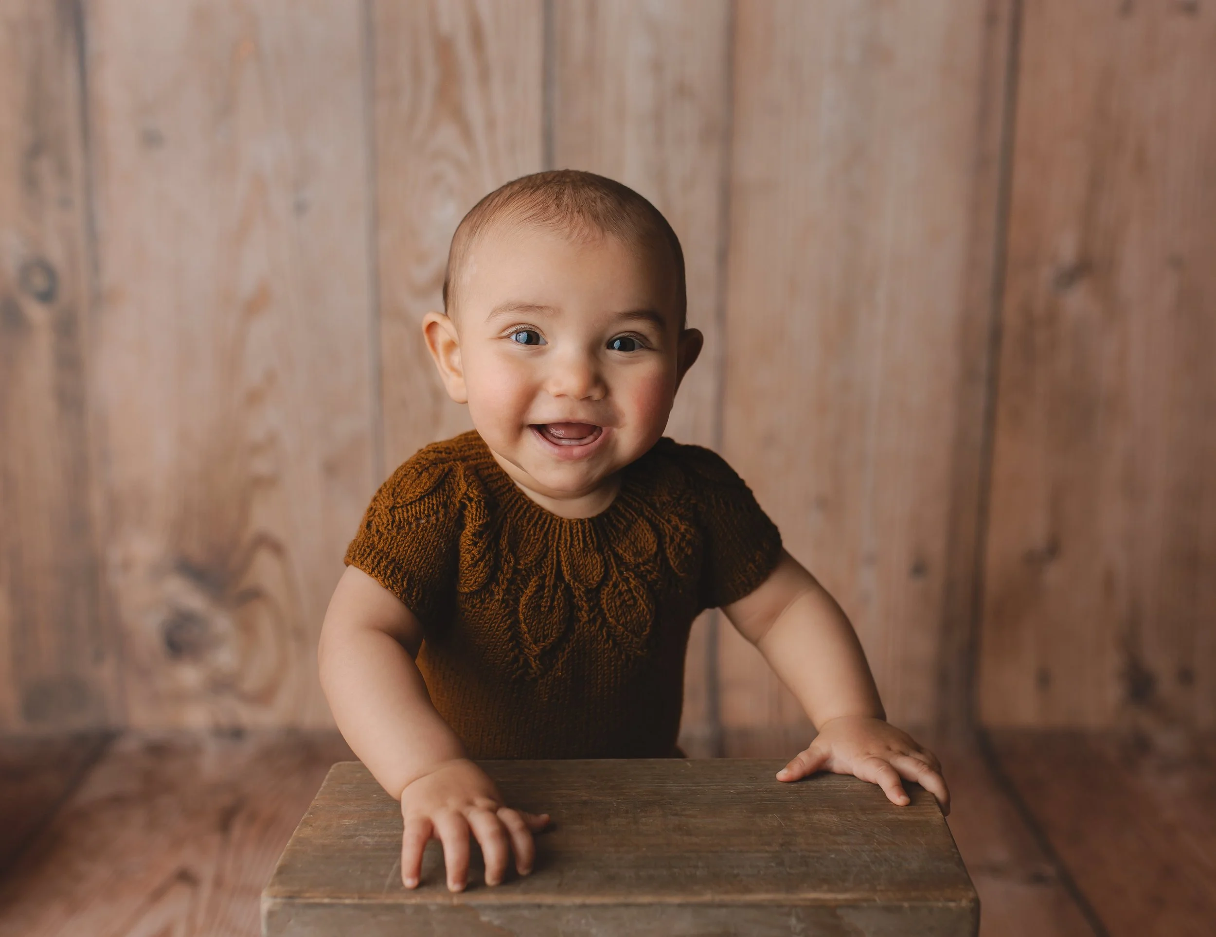 Smilende baby med kort hår som holder seg på en treplate, mot en trevegg.