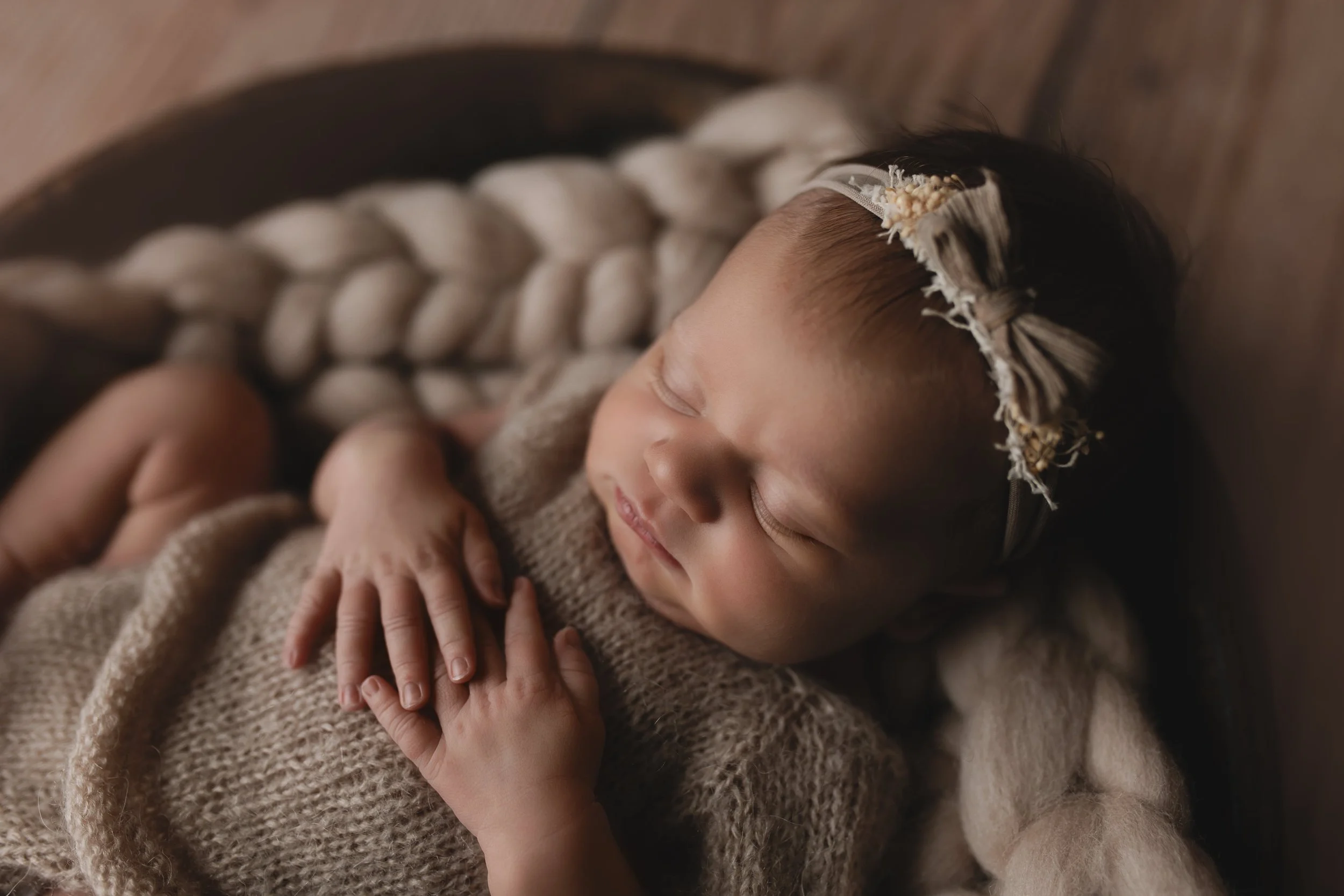 Søvnende baby med blomsterhodeband, som ligger i en rund kurv med ullfilt