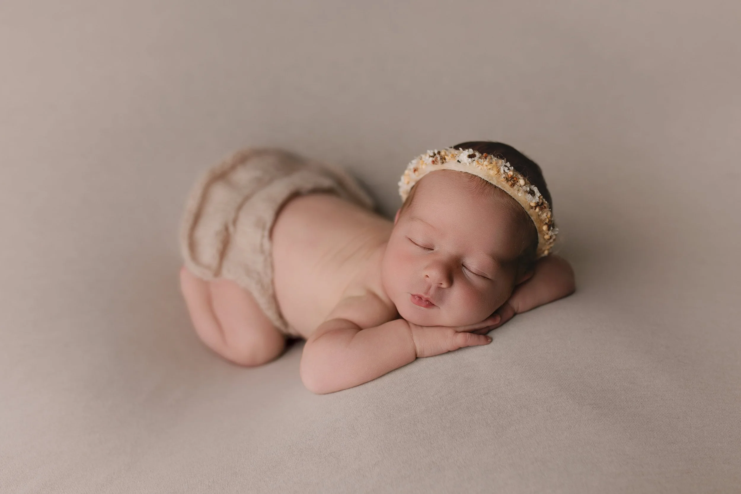 Søvnende baby med hodebånd på hodet, liggende på siden på en myk, lys bakgrunn.