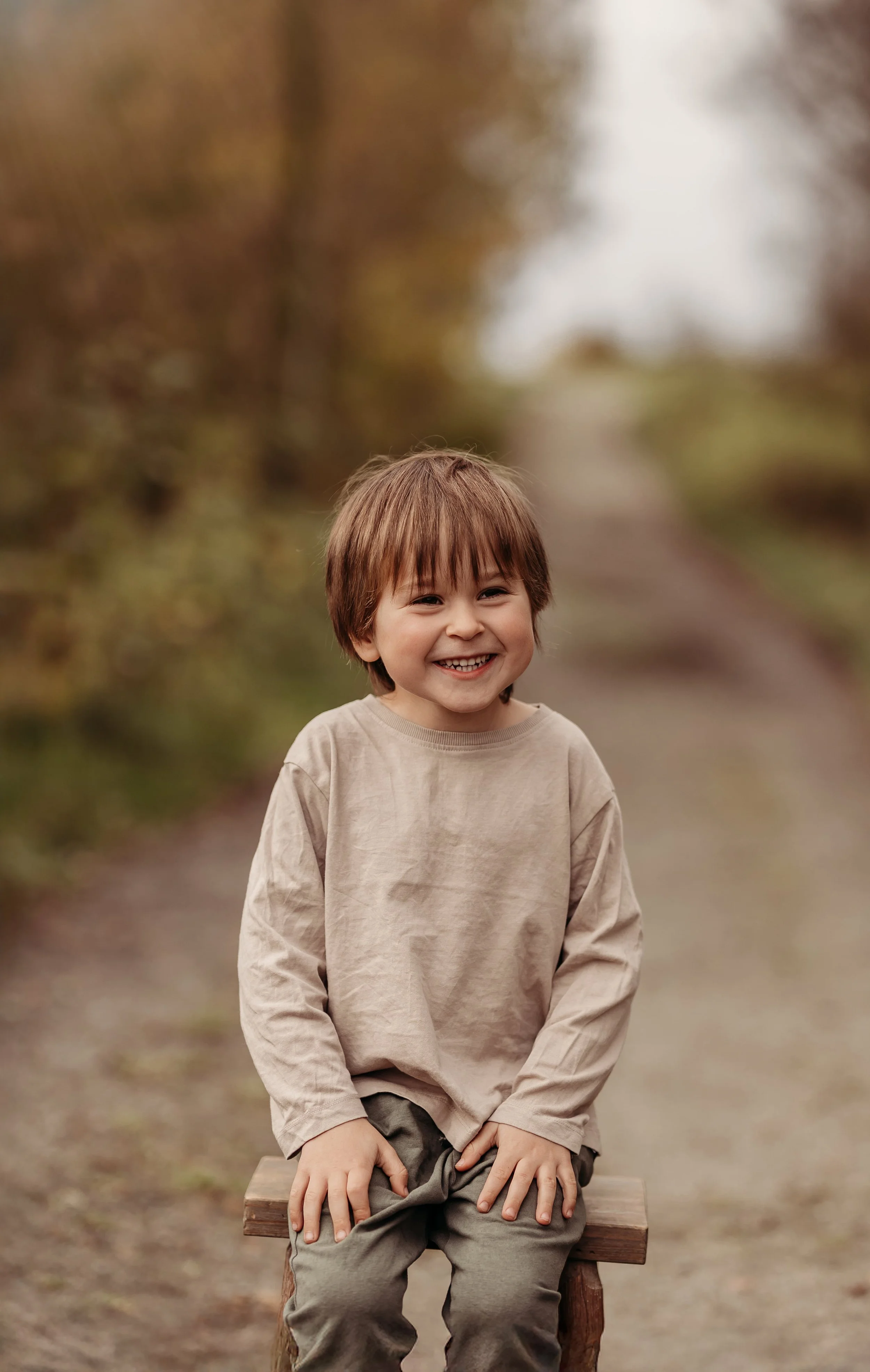 Ung gutt som ler og sitter på en benk utendørs, med høstfarger i bakgrunnen.
