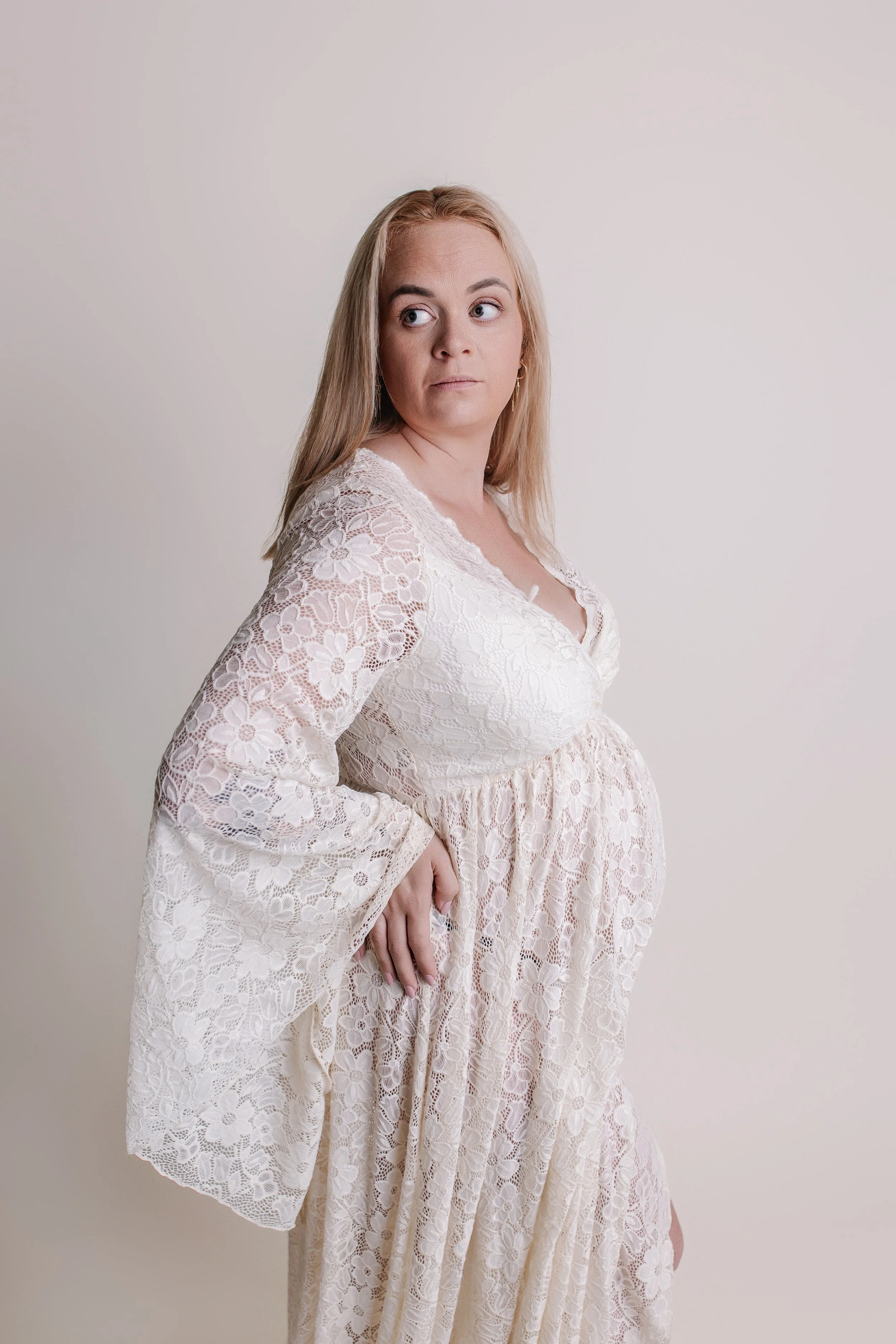 En gravid kvinne med langt blond hår iført en lys, blonder kjole.