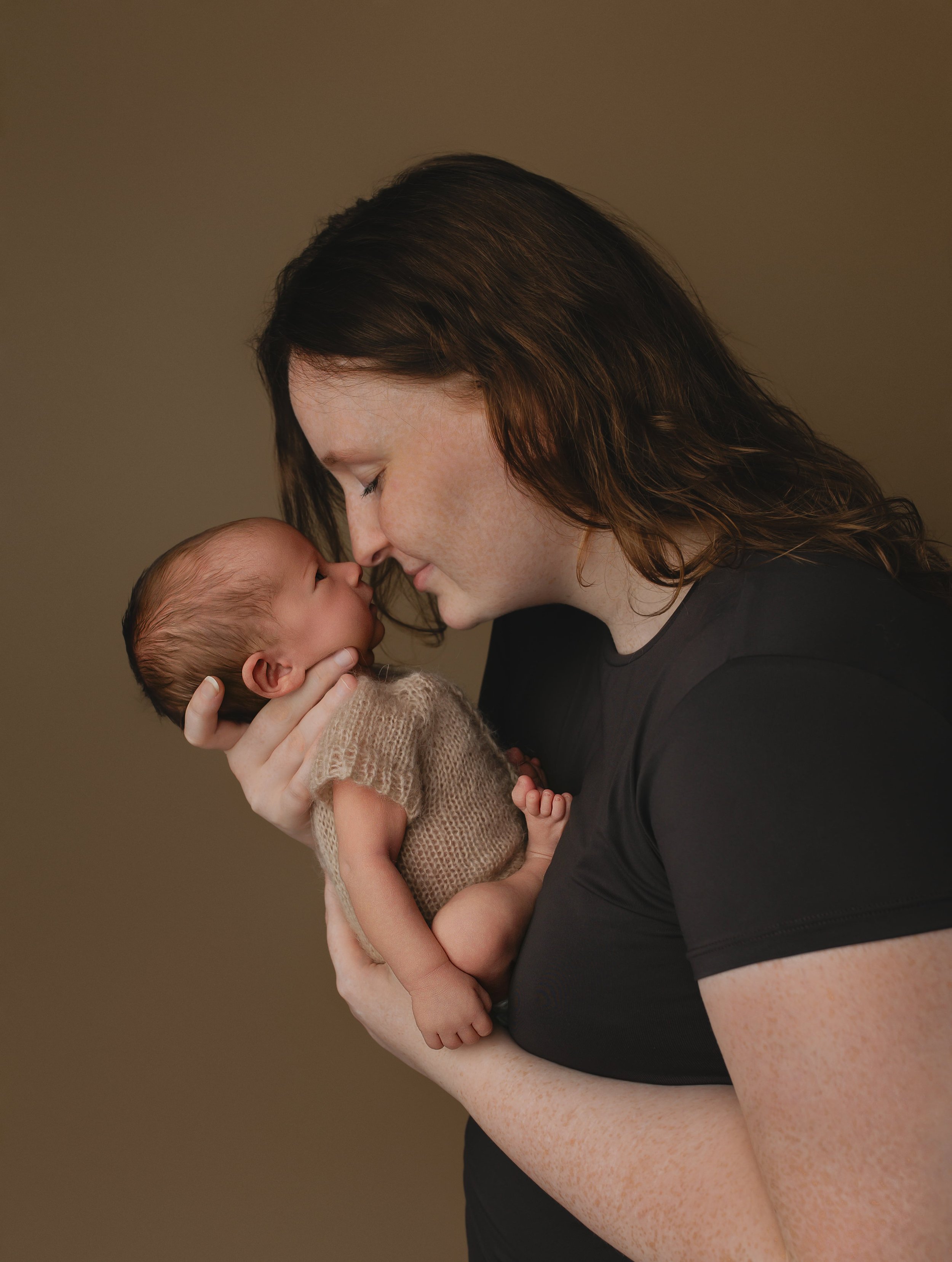 Et bilde av en kvinne som holder en nyfødt baby nært og kjærlig, begge med nesene nesten berørende.