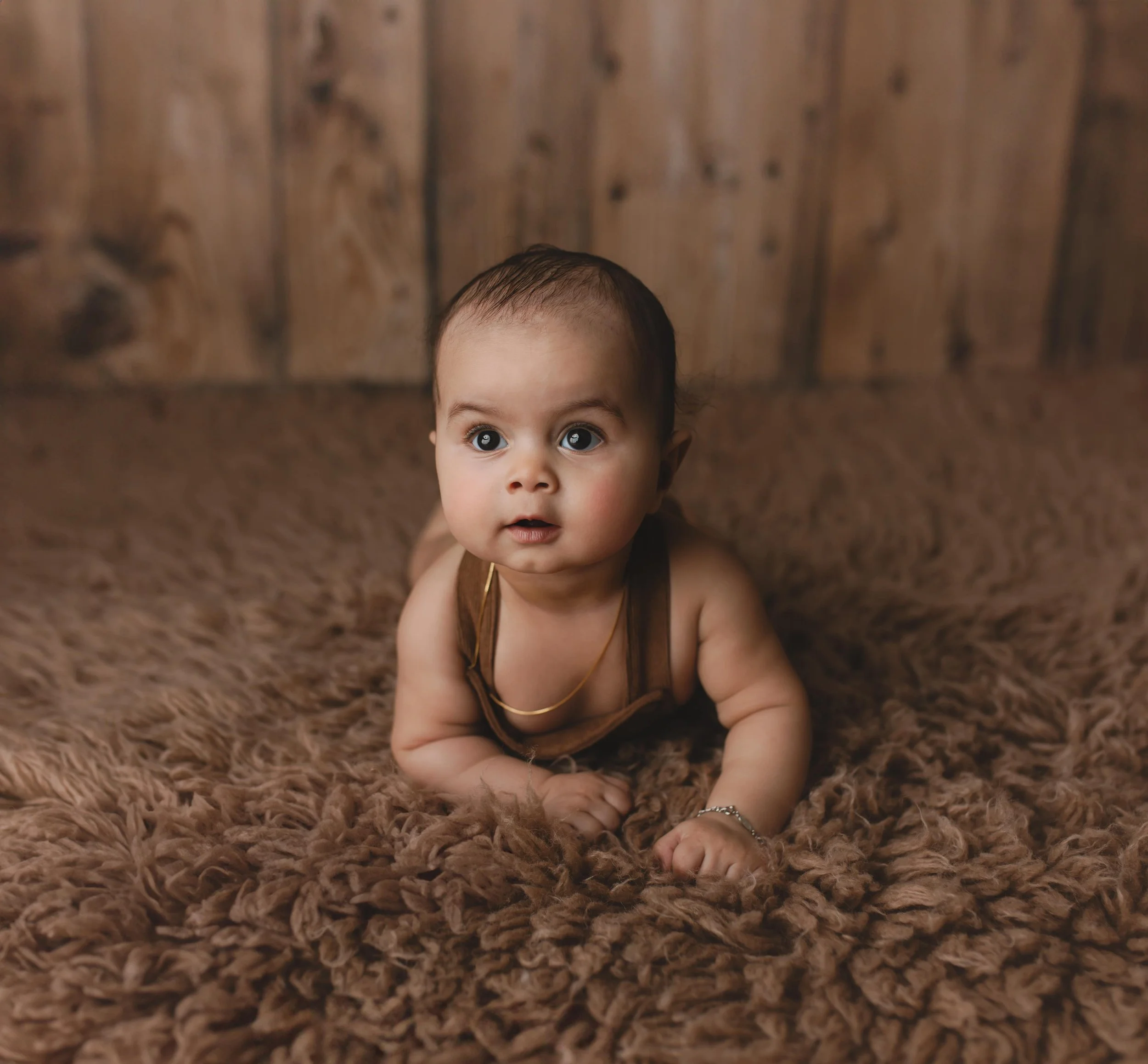 Baby som ligger på en brun, fluffy teppe med en bakgrunn av trepanel.