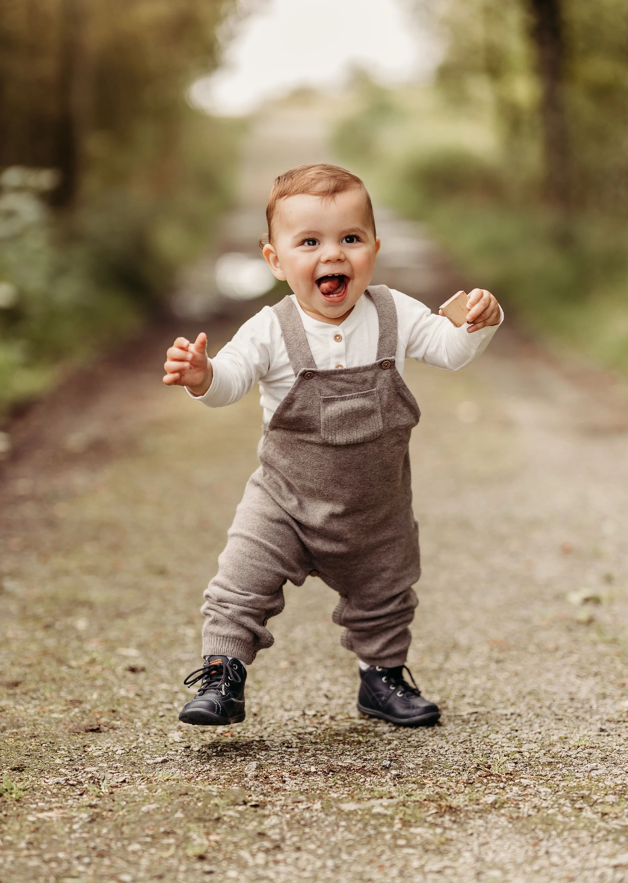 En liten gutt som går på en skogssti, smilende og holder en bit brød i hånden.