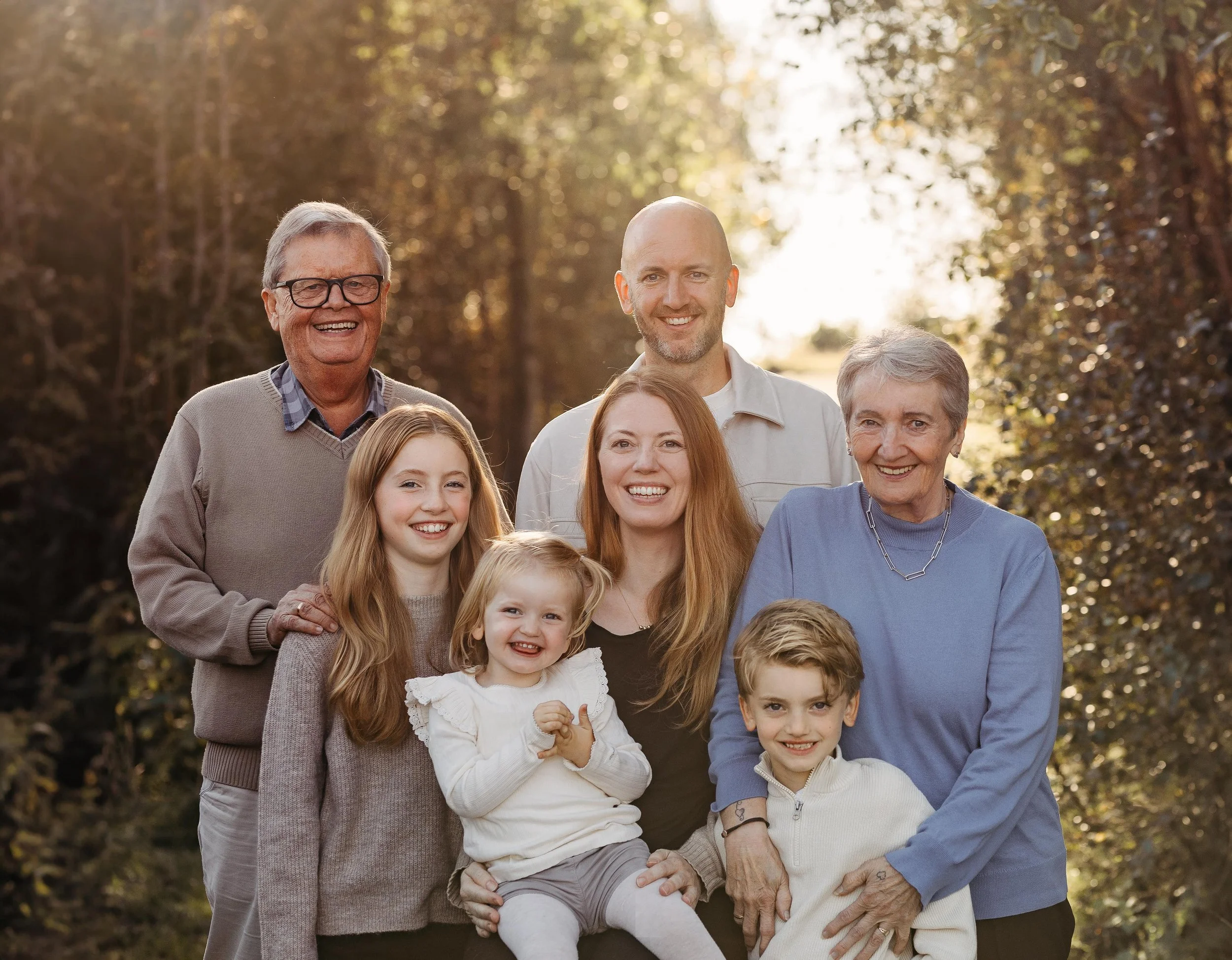 En familie på åtte smiler og poserer utendørs i en skog om høsten
