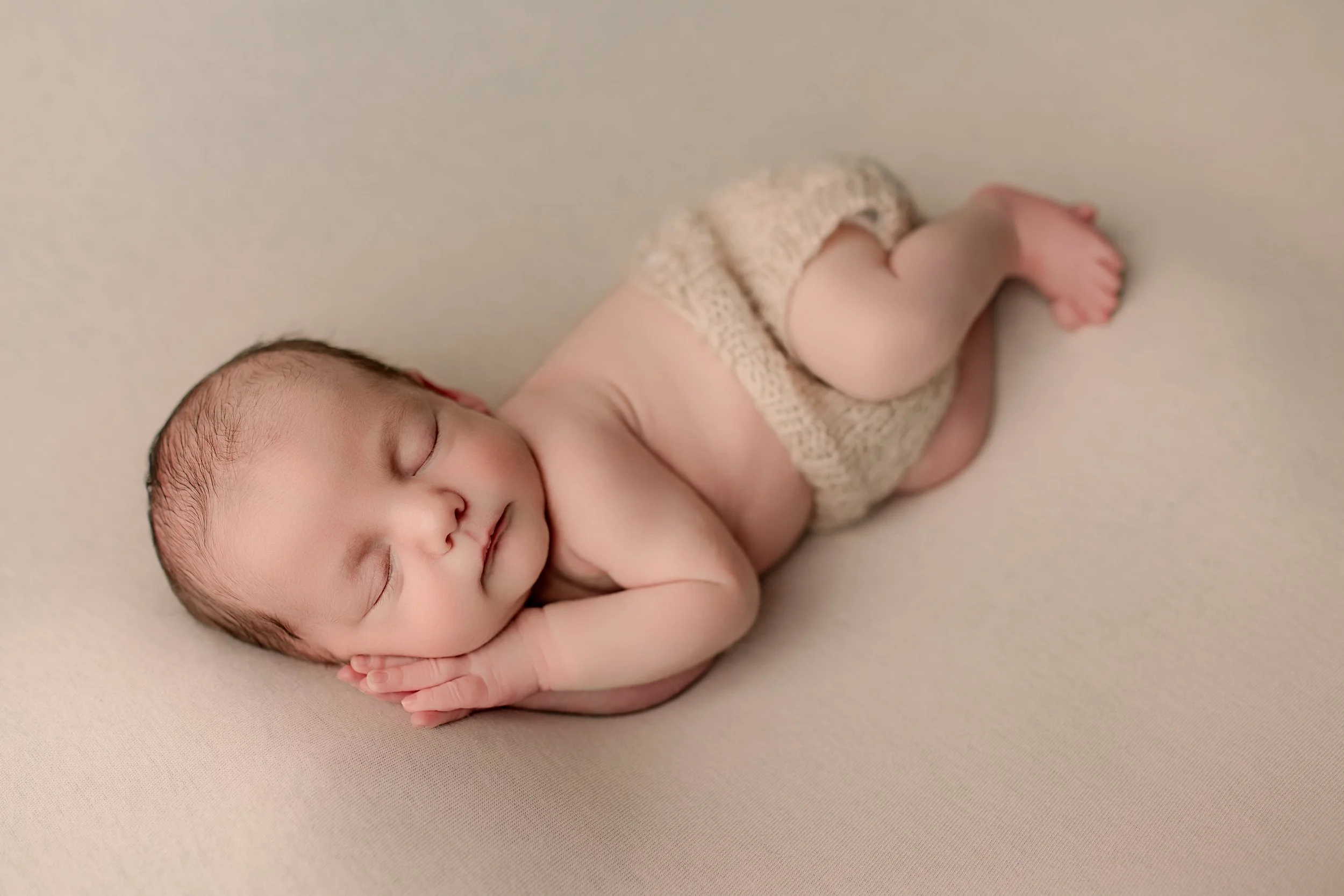 Sovende baby med beige bleie ligger på en lys bakgrunn.