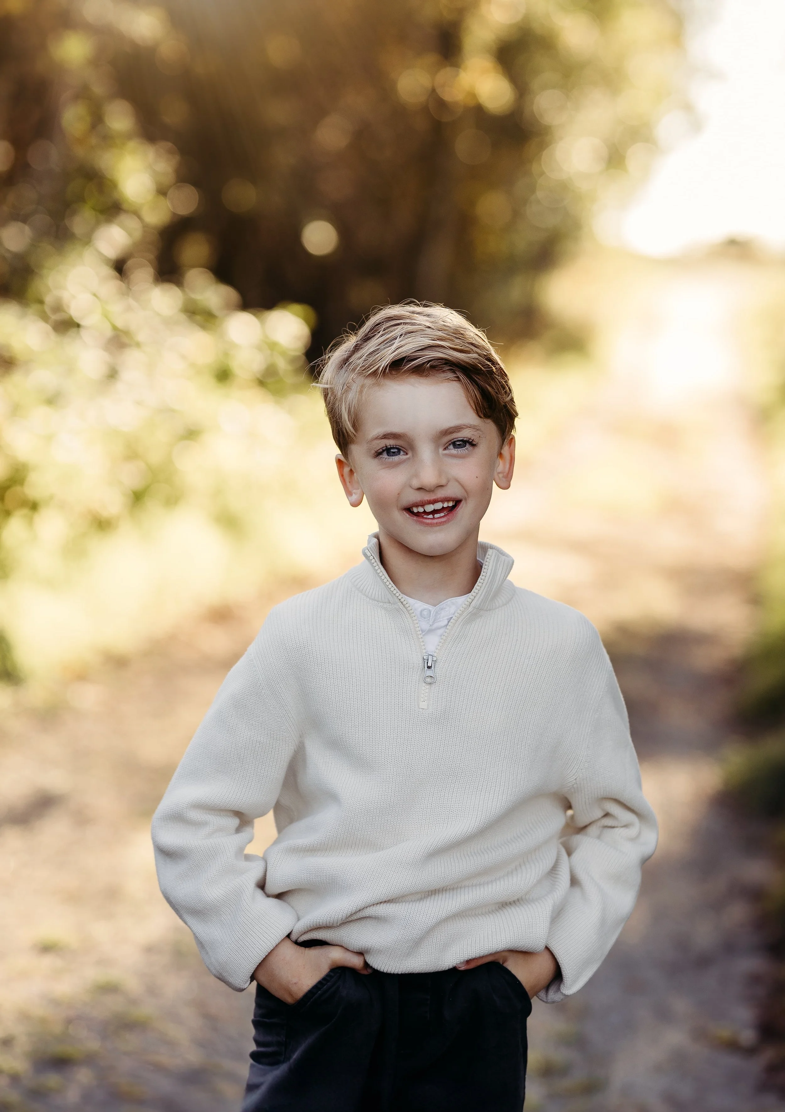 En ung gutt smiler på en sti i naturen med sollys i bakgrunnen.