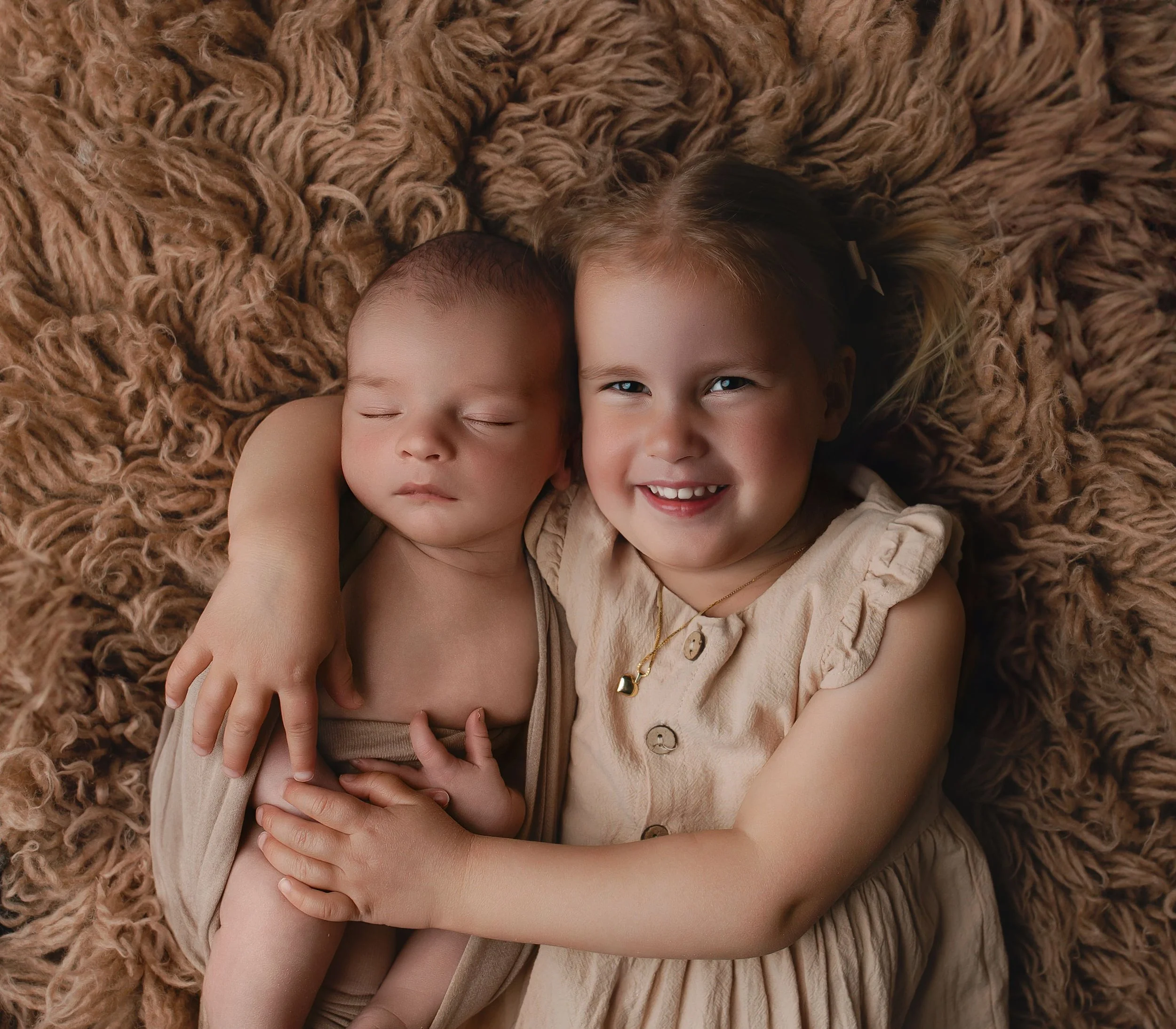 To barn, en som sover og en som smiler, ligger på en myk, brun pelsaktig pute.