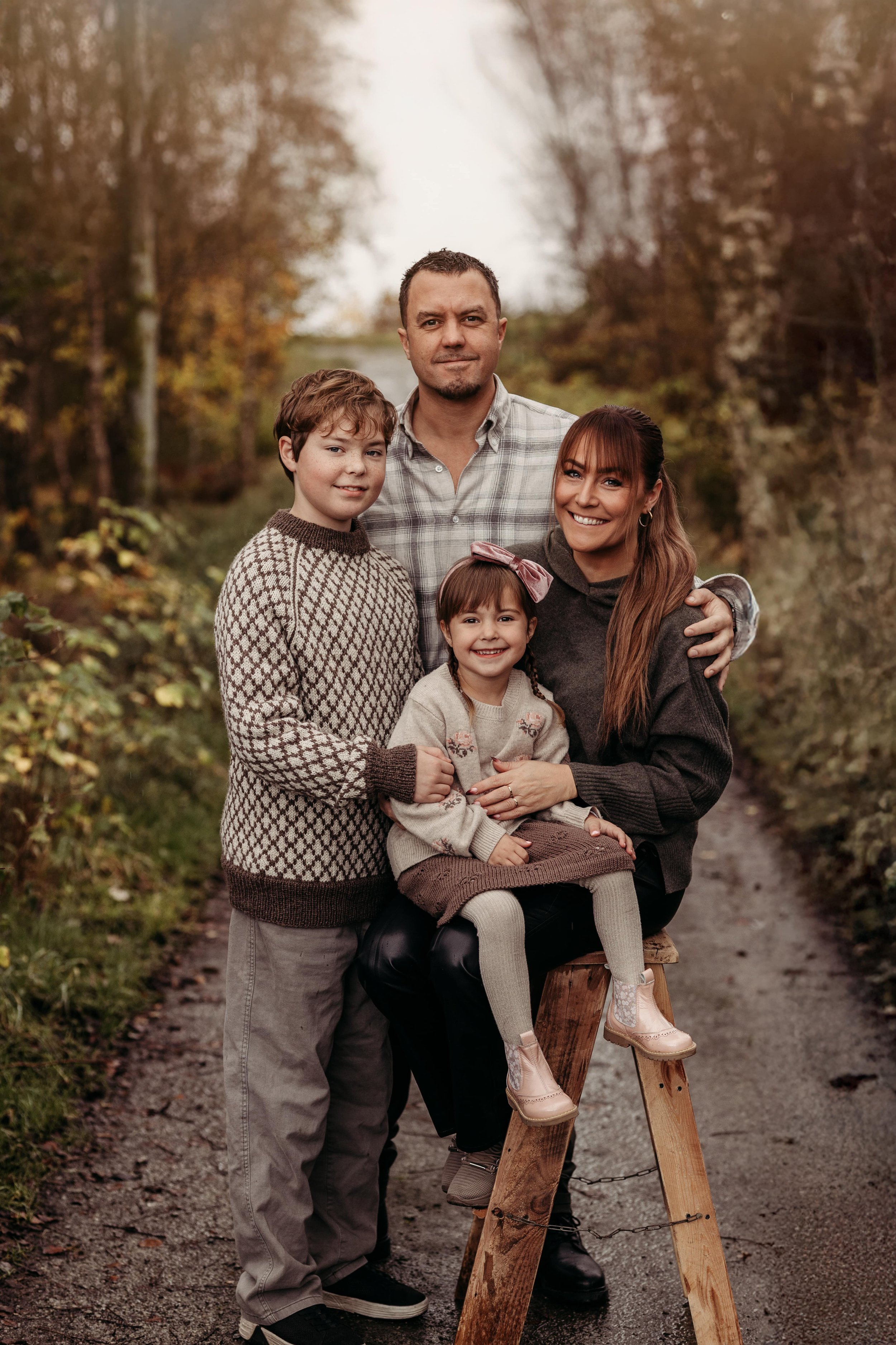 En fornøyd familie på fire som står og sitter på en sti omgitt av høstløv og trær.