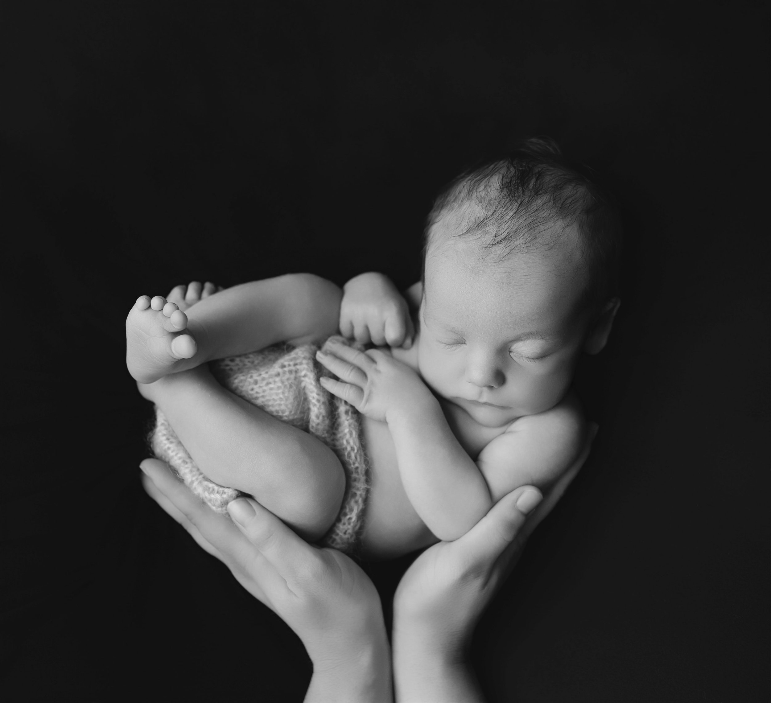 Sort-hvitt bilde av en sovende baby som holdes i hender.