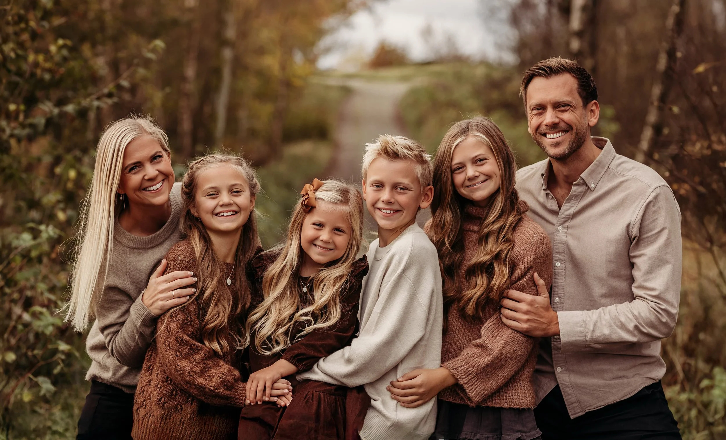 En familie på syv smiler og står sammen utendørs i høstlandskap.