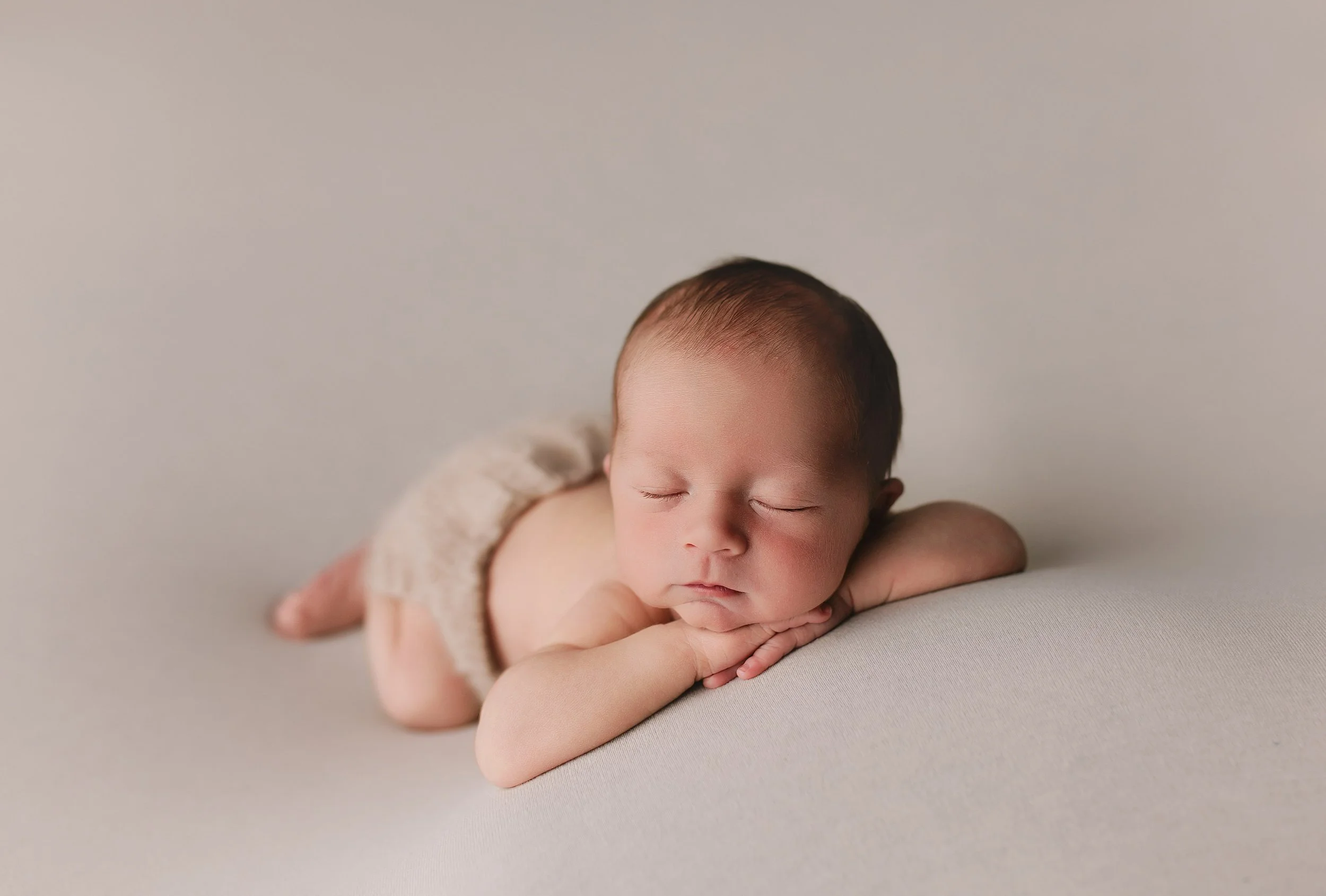 Søvnende baby liggende på magen med hånd under haken, isolert på lys bakgrunn.