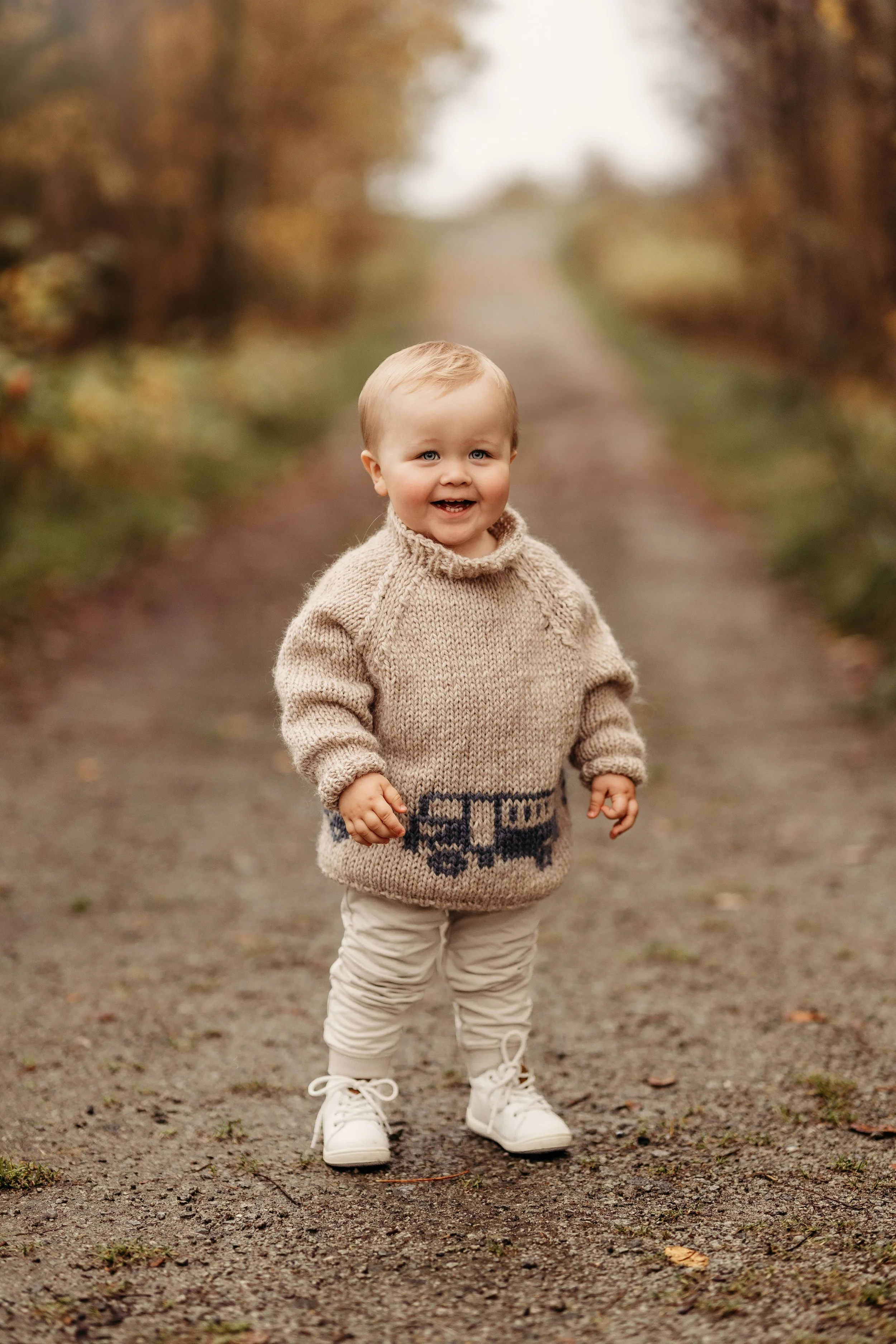 En liten gutt i håndlaget genser med togets design, på en skogssti om høsten.