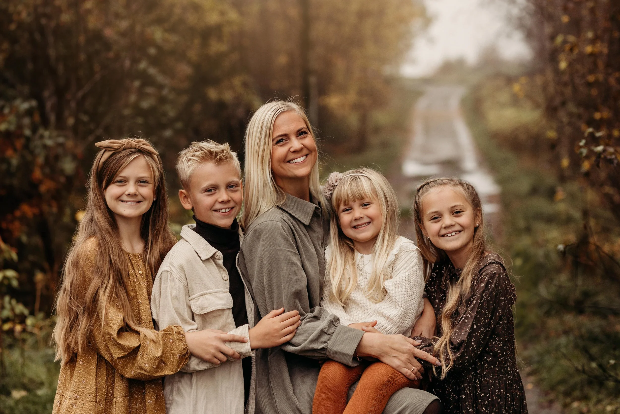 En kvinne og fem unge jenter som smiler og koser seg i en skog under høsten.