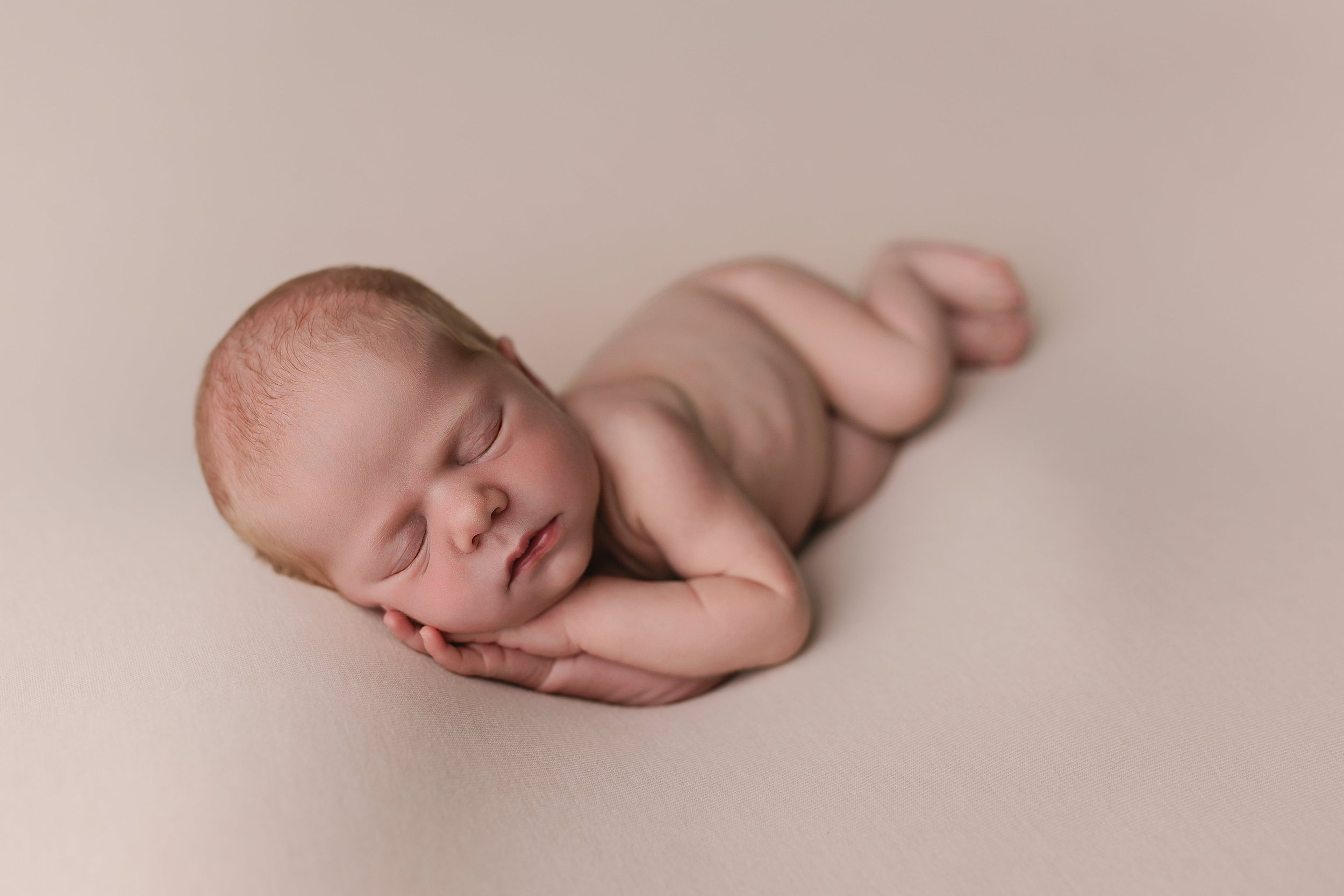 Nyllommet baby som sover på en lysfarget bakgrunn, ligger på siden med hodet støttet av en hånd.