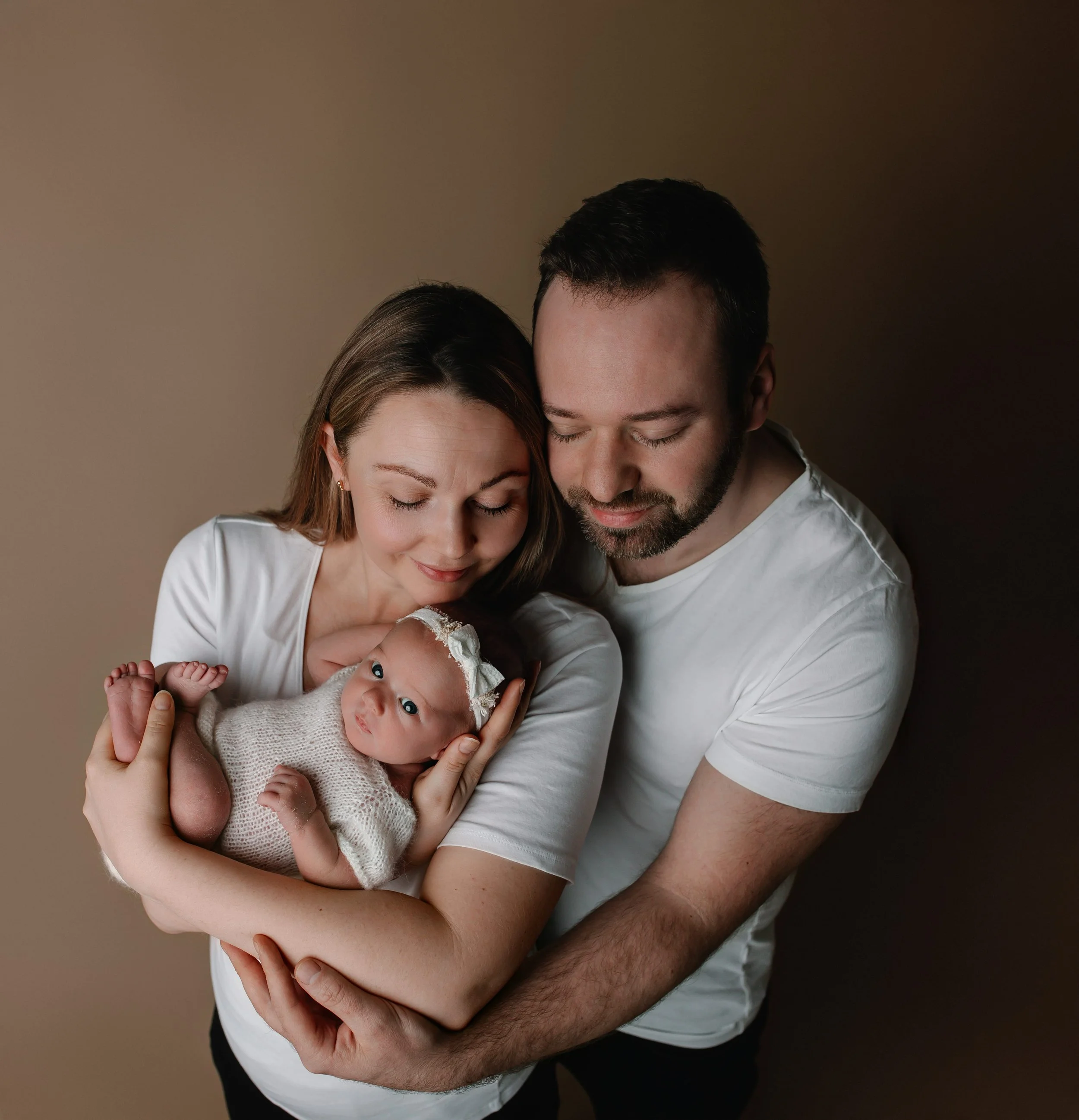 En lykkelig familie med to voksne og en nyfødt baby, som holder og ser på barnet.