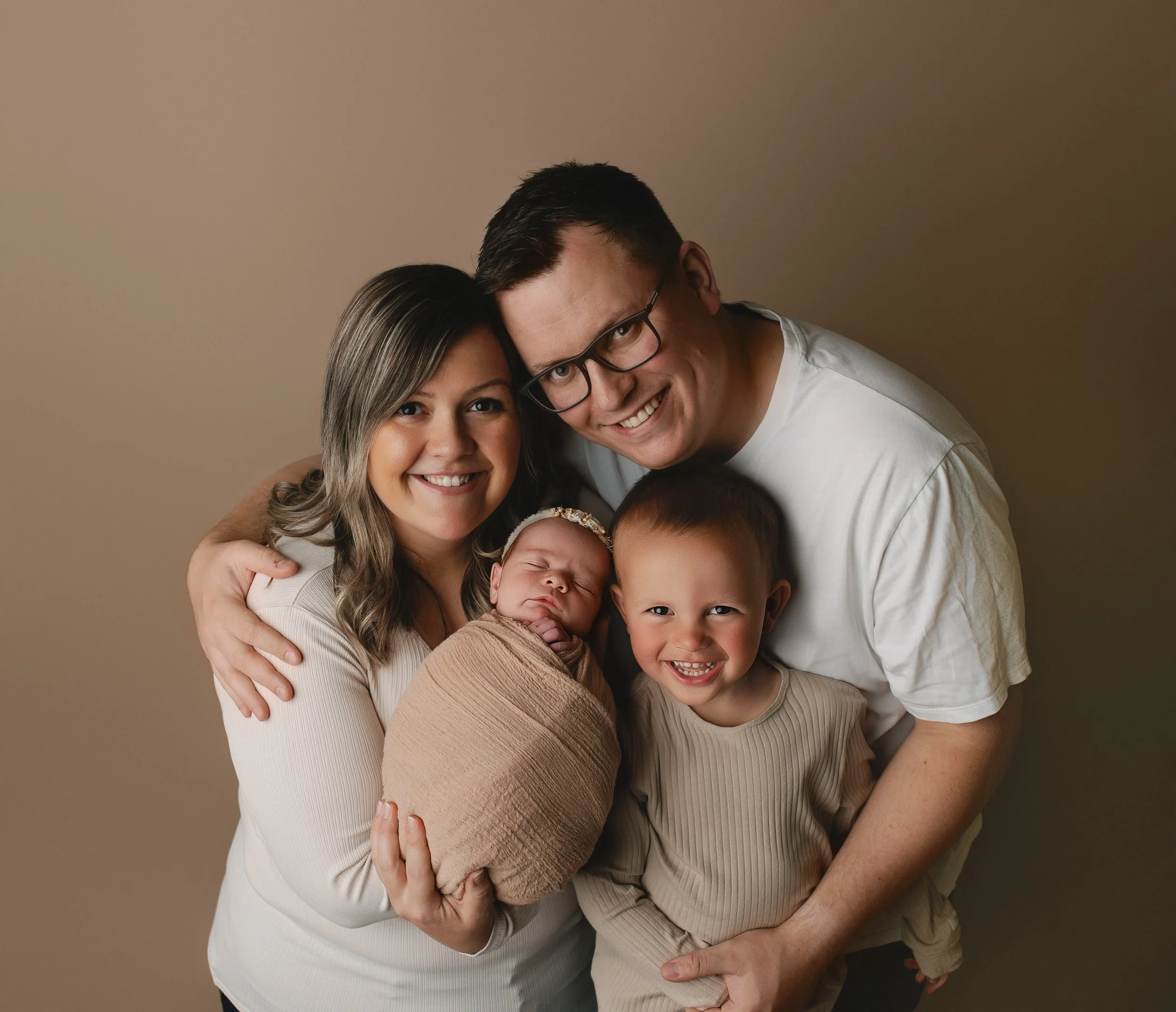 Familie med to voksne, en liten jente og en baby, smiler og koser seg sammen.