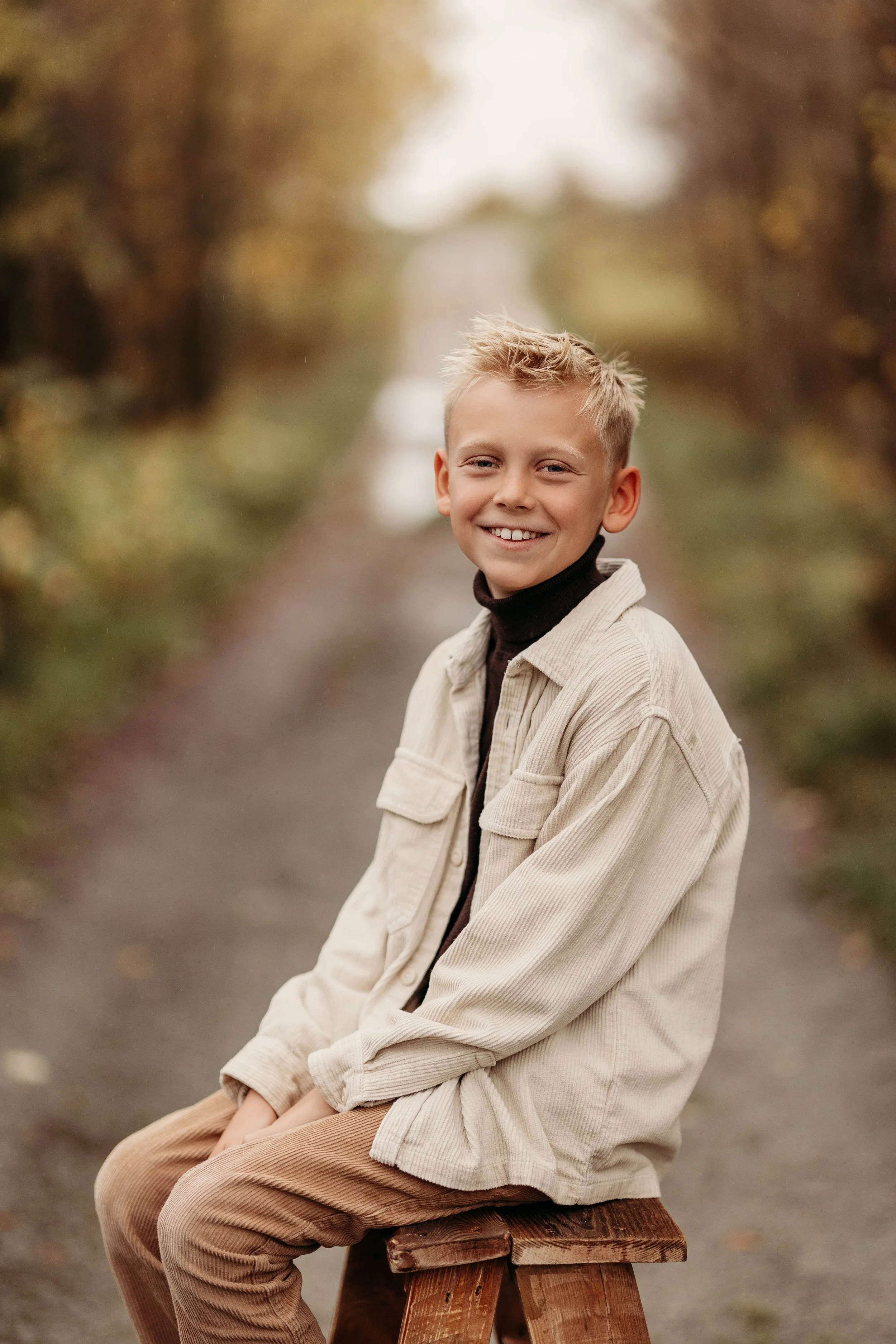 En ung gutt som sitter på en trebakke på en sti omgitt av høstfargede trær.