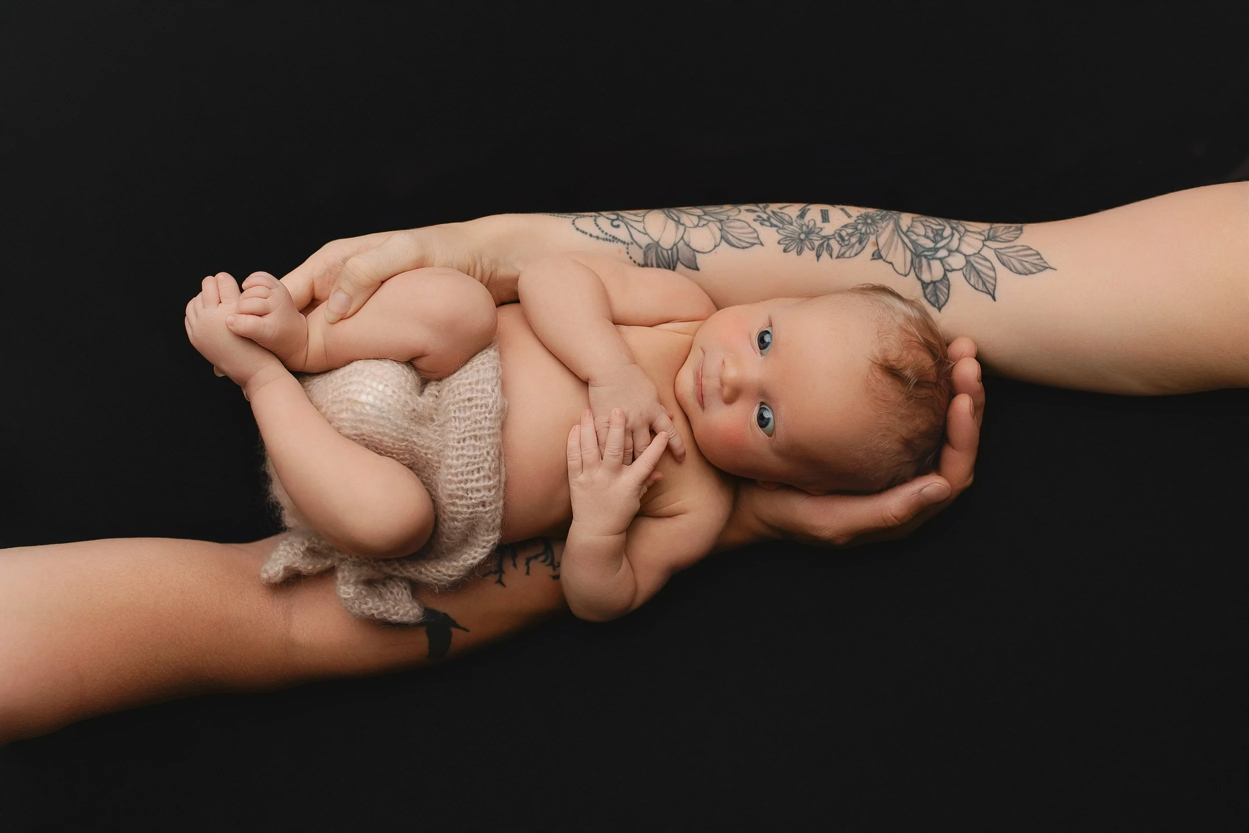 En nyfødt baby som ligger på en persons arm mot en svart bakgrunn.