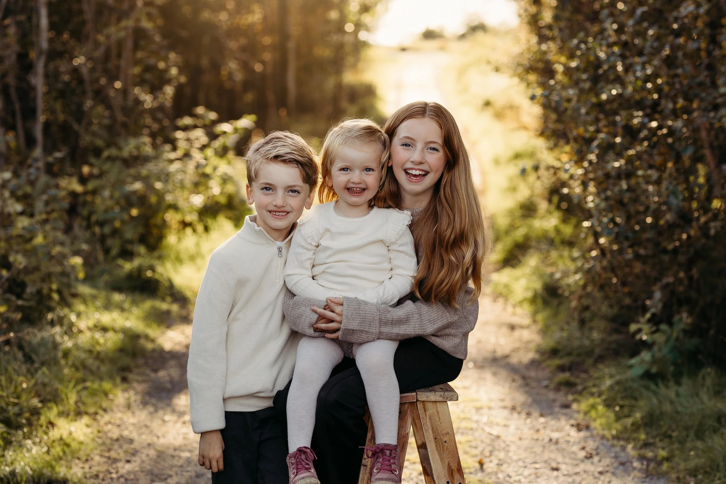 En gruppe på tre personer som smiler og koser seg ute i en vakker, solrik skog med grønne busker.