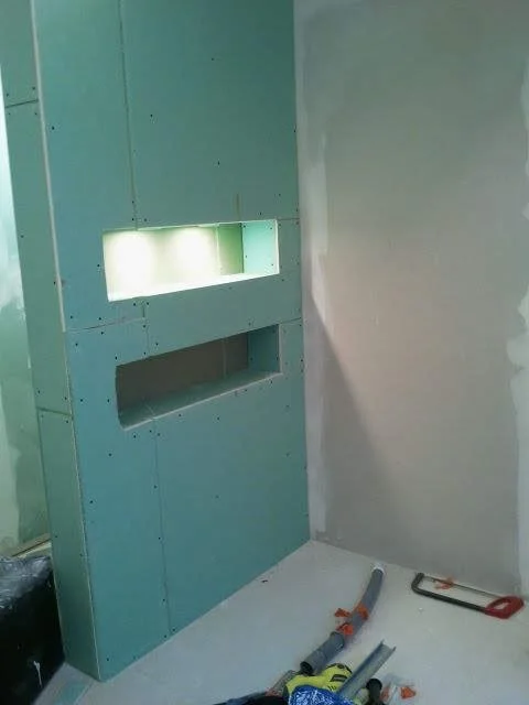 Cloison en plaque de plâtre en cours de construction, avec une ouverture rectangulaire et un éclairage intégré, dans une pièce en travaux.