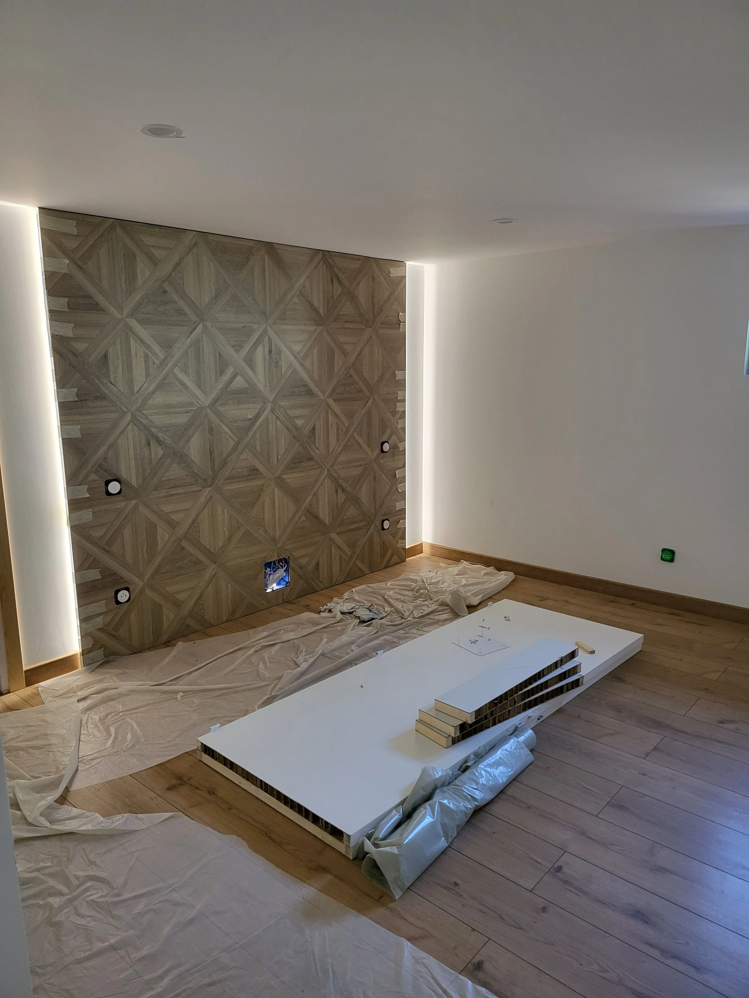 Salle de séjour en cours de rénovation avec un mur en bois, un sol en parquet, des couvertures et un panneau blanc à assembler.