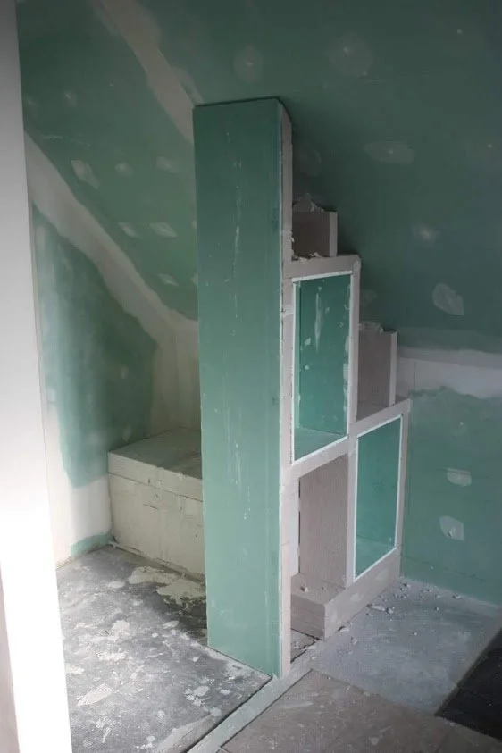 Une cloison en construction avec des cadres en bois et des vitres, dans une pièce en cours de rénovation.