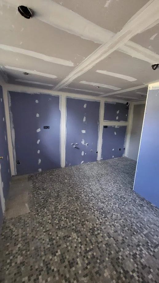 Pièce en cours de rénovation avec murs en placo en cours de finition et sol en mosaïque.