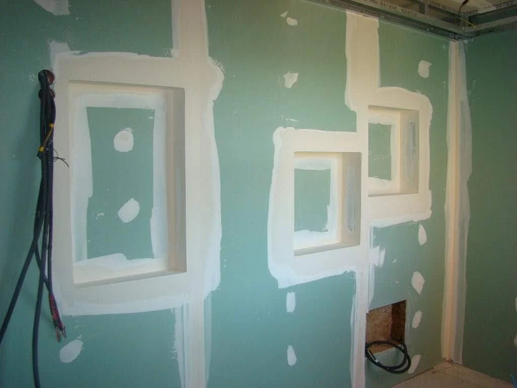 Mur en cours de construction avec des cadres en bois encastrés, murs en plaques de plâtre en cours de finition.