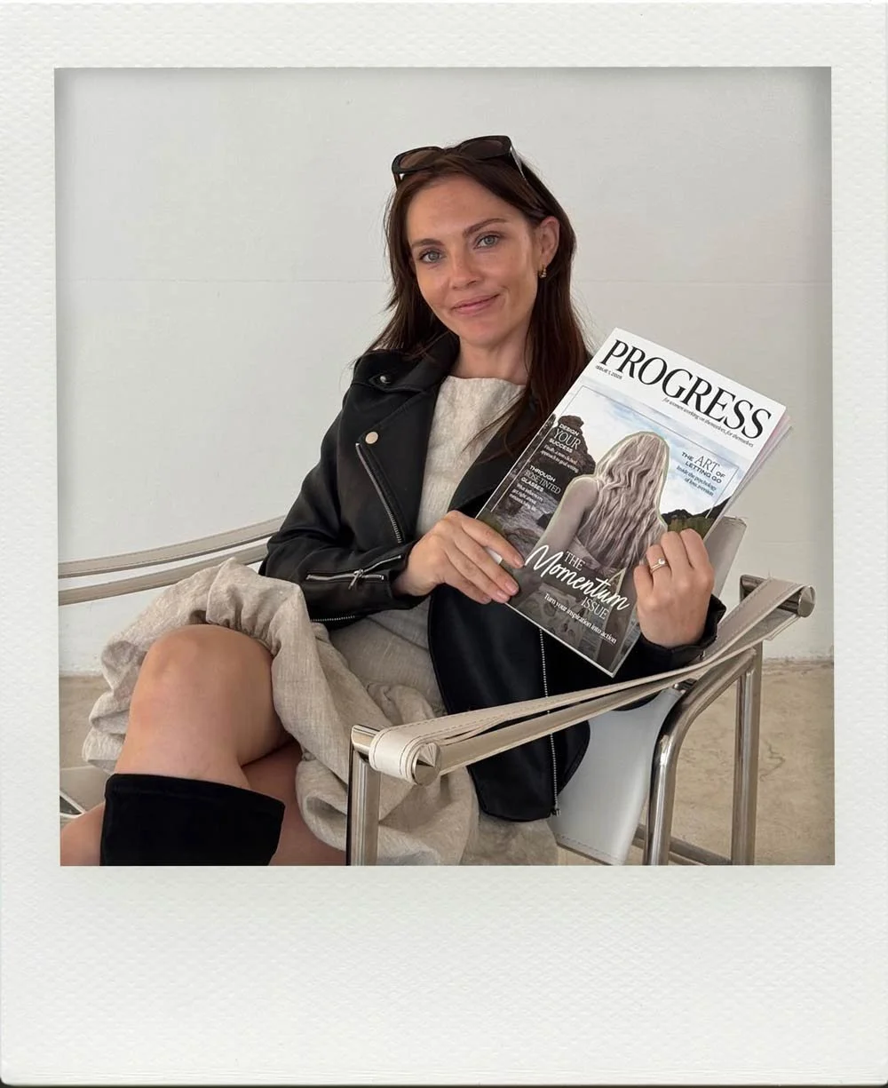 Emma Clark-Norris seated in a chair and holding up the first published issue of her magazine, Progress in 2025.